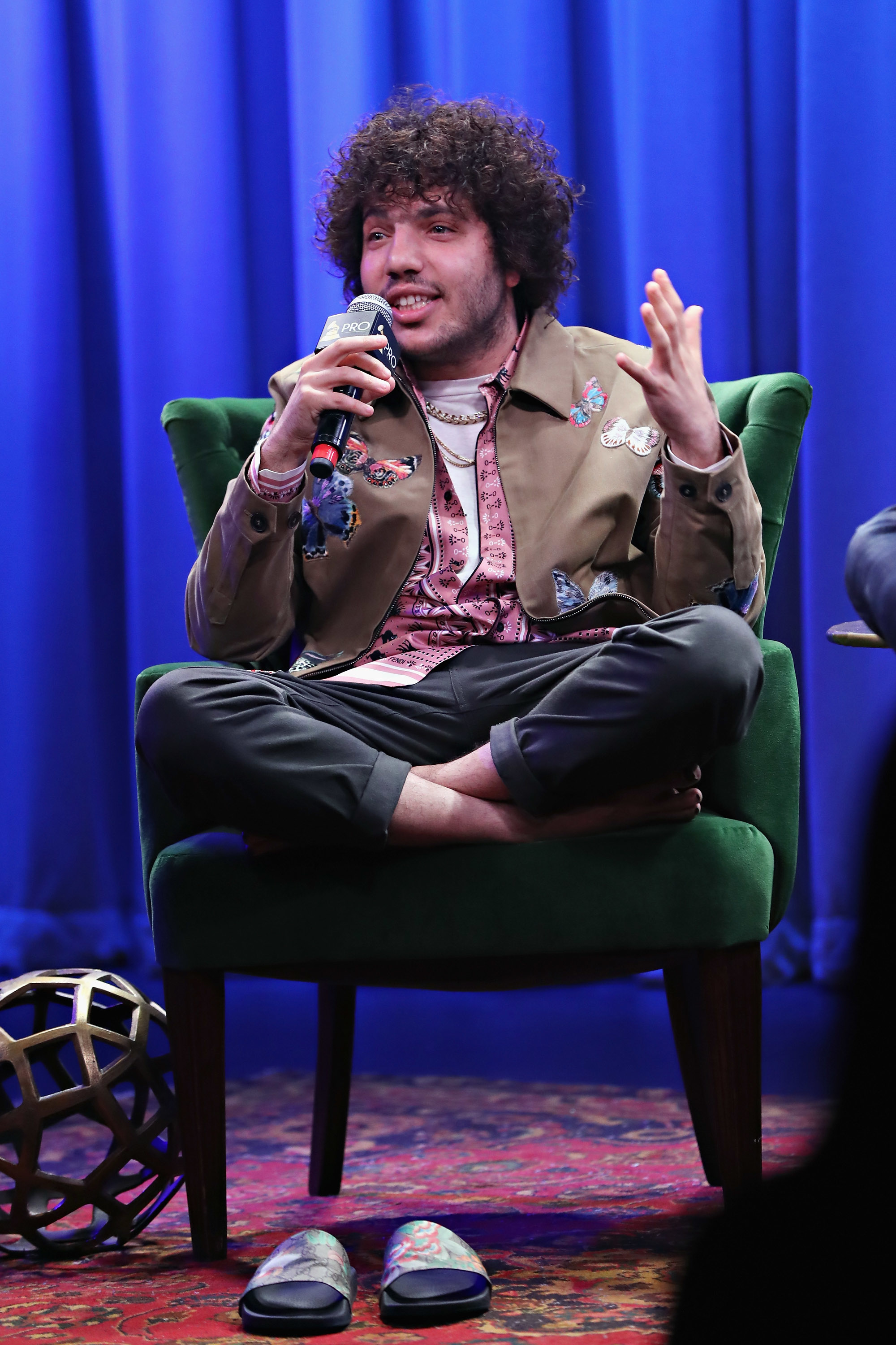 Close-up of Benny sitting cross-legged in a chair and holding a microphone