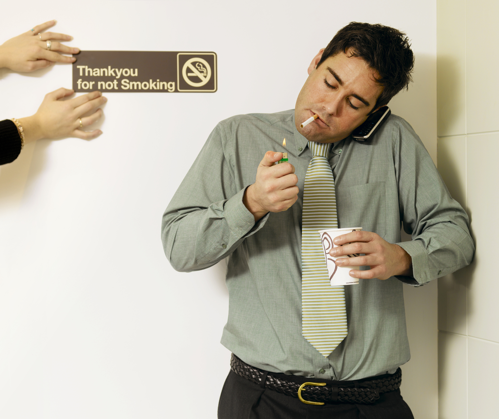 person lighting a cigarette by a no smoking sign