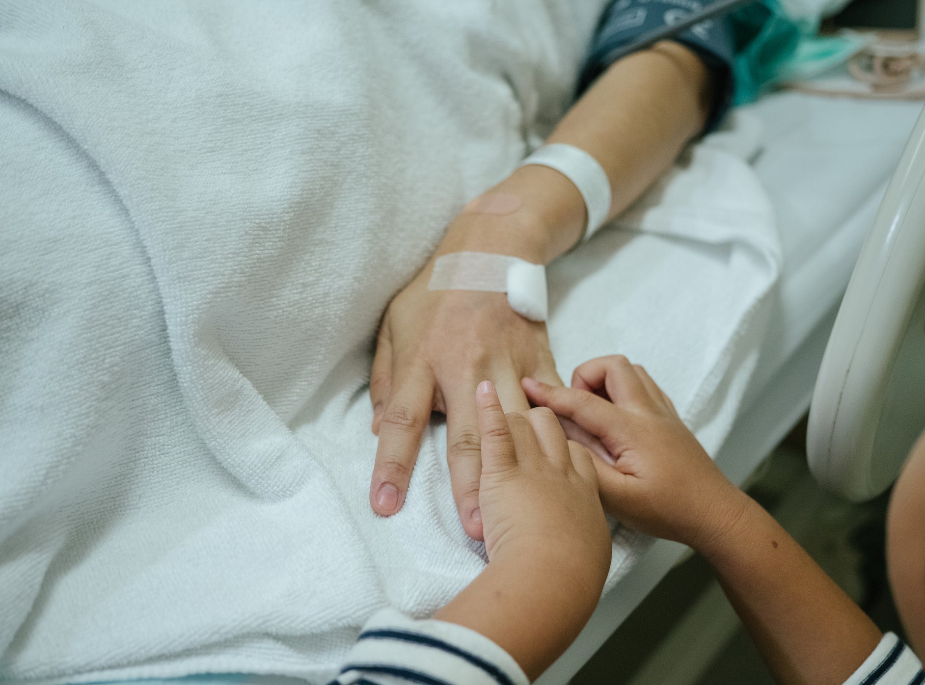 kids hands holding the hand of someone in a hospital bed