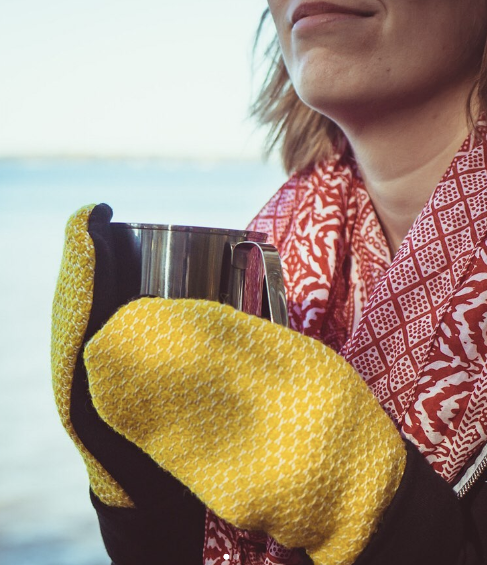 A woman holds a mug with two hands, both sporting cozy hand knit mittens.