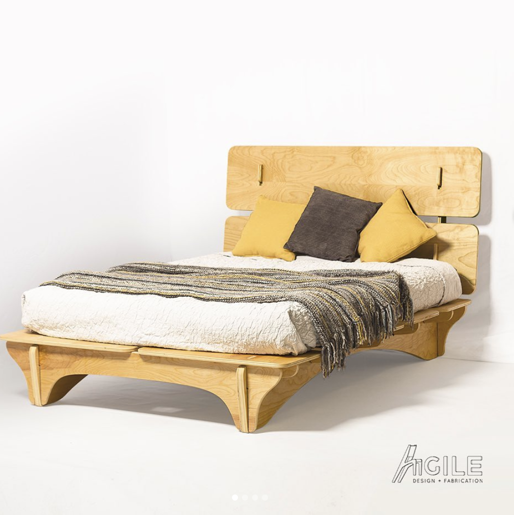 A light wood bed frame with a cozy blanket overtop the mattress.
