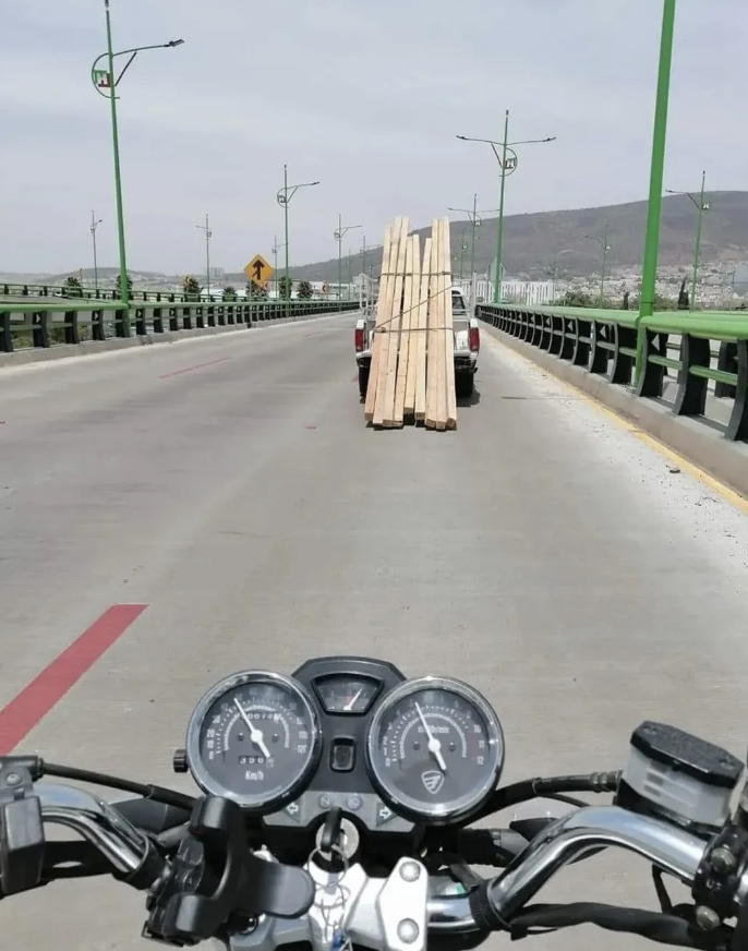 View from a motorcycle with a truck with boards in front of them
