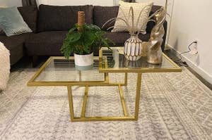 a reviewer photo of the gold and glass coffee table with a plant and decor on top