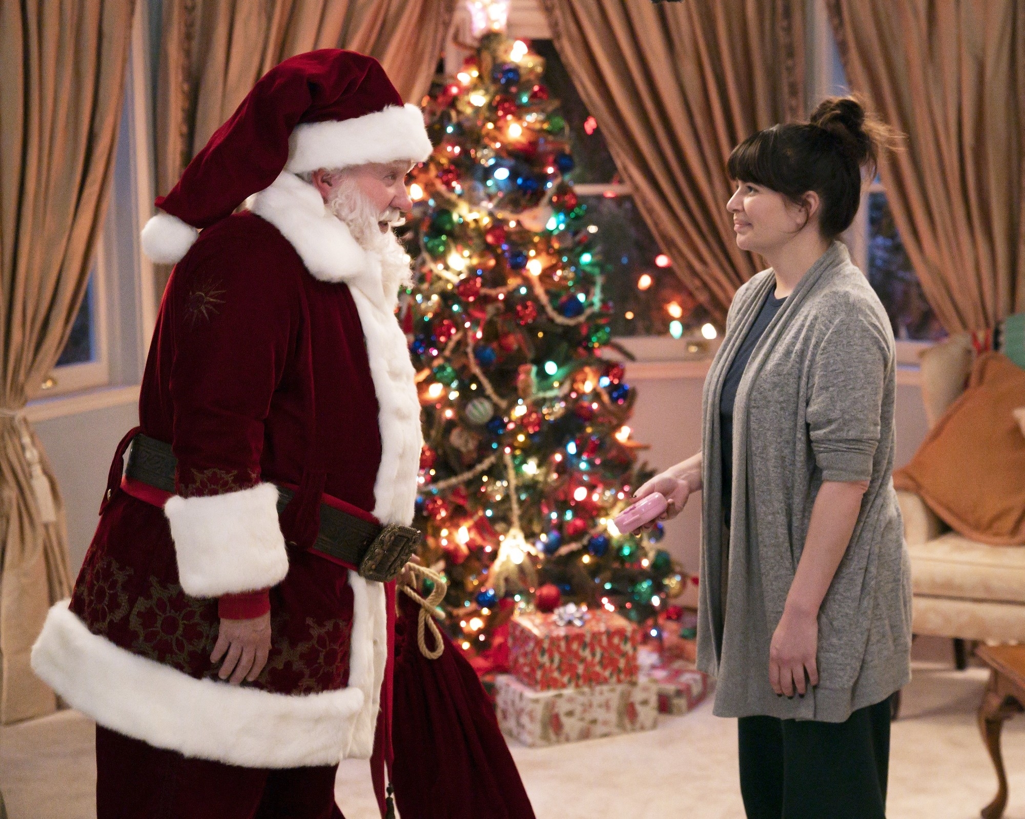the two standing in front of each other in a scene where tim is dressed as santa in front of a christmas tree