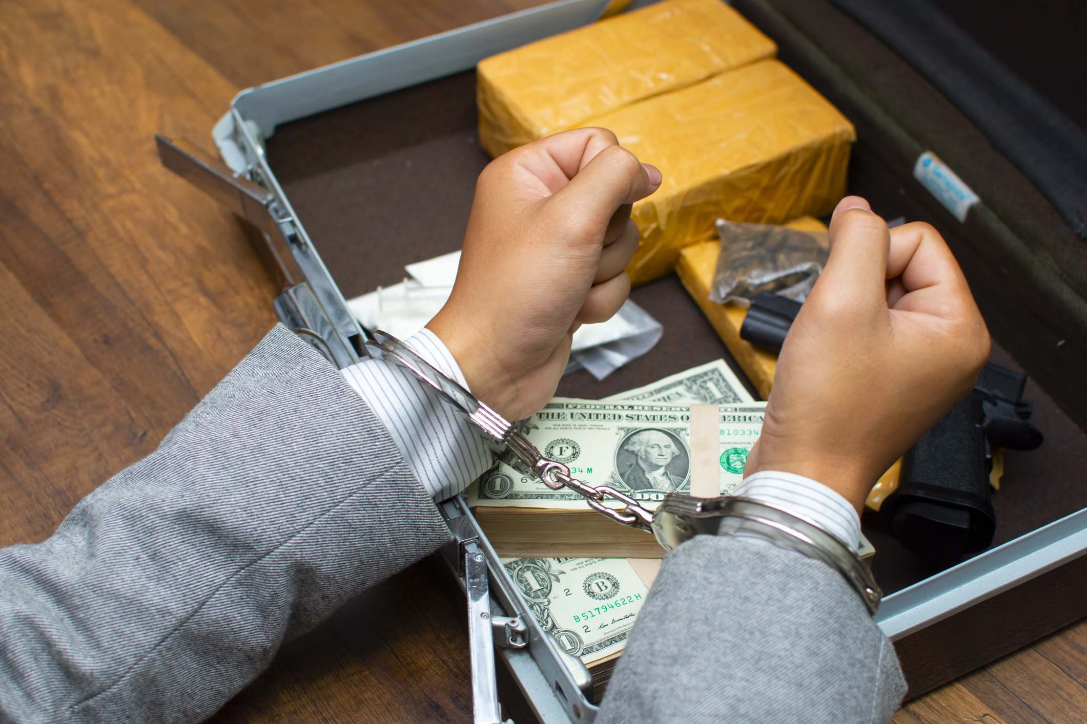 a person handcuffed over a brief case with drugs and money