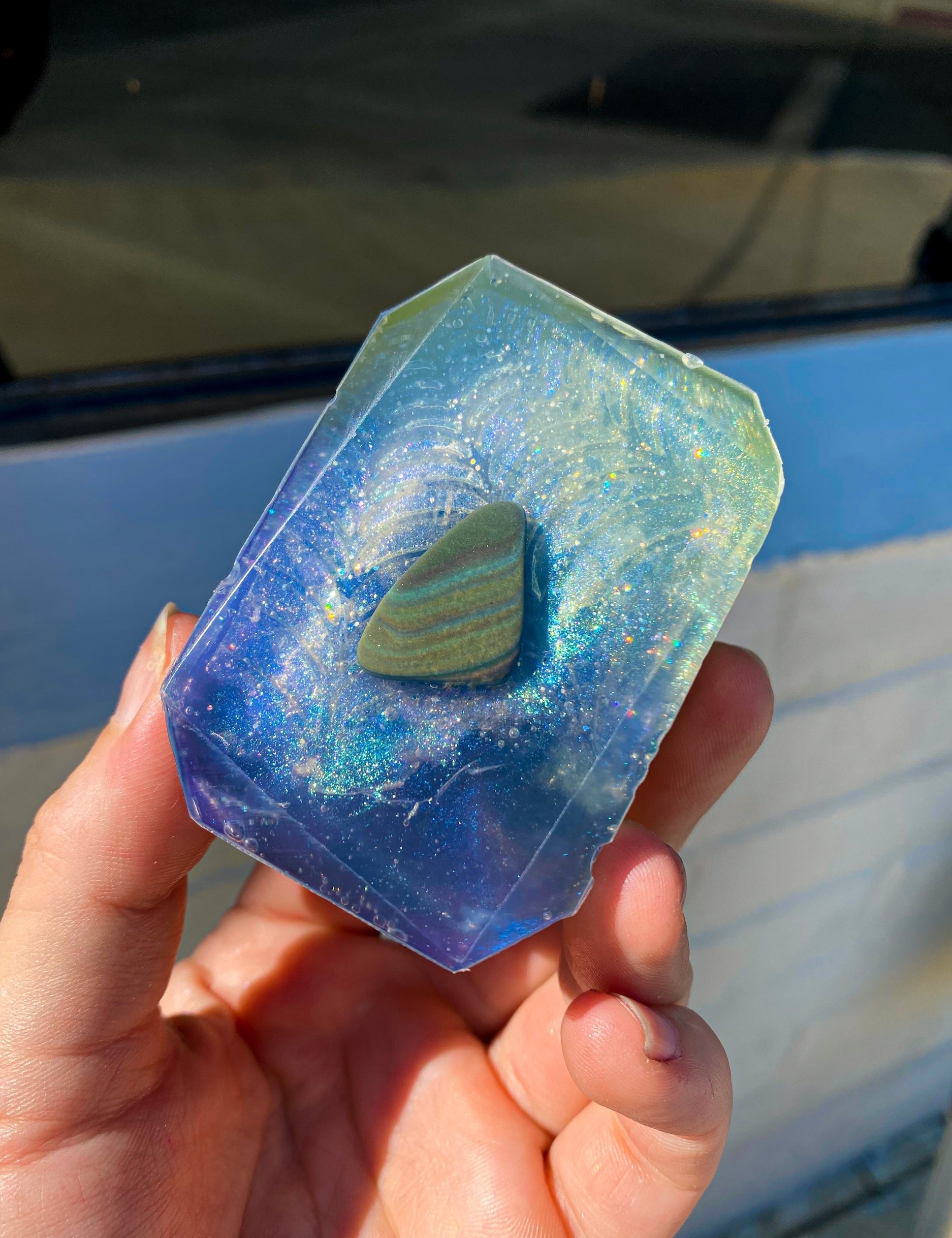 The bar of teal and blue soap with opalescent glitter, plus the Rainbow Obsidian crystal in the center
