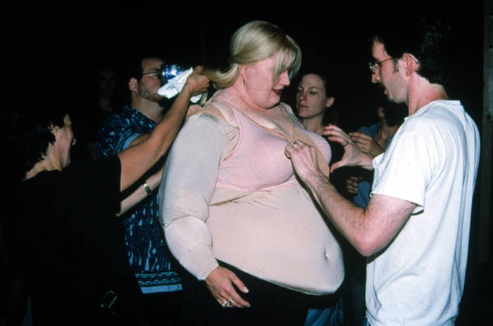 A director helping an actor adjust their bra while wearing a fat suit
