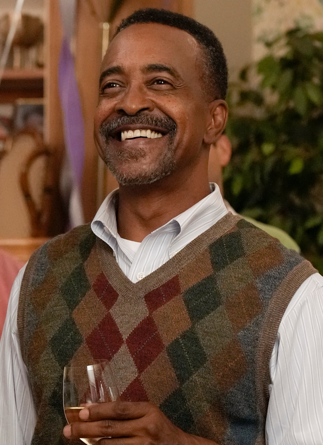 closeup of him wearing the same sweater vest and holding a glass of wine