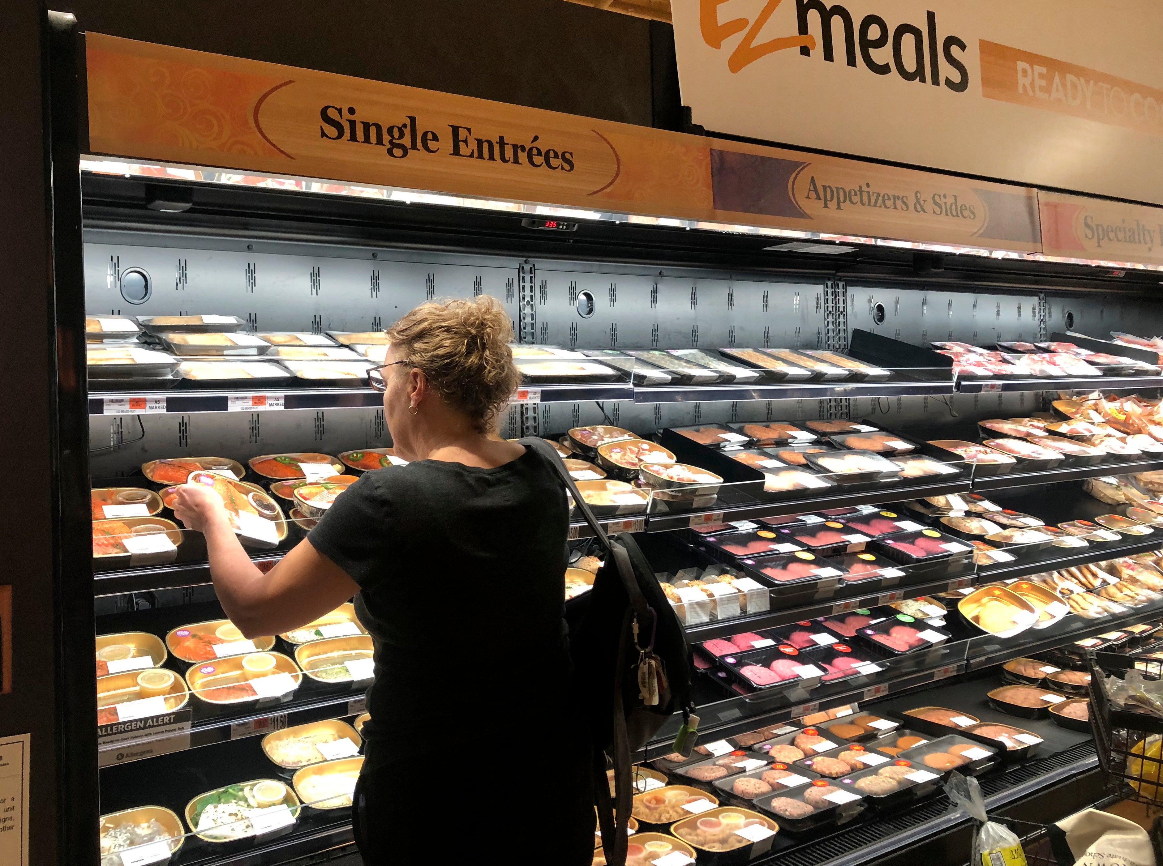 Woman selecting from assorted prepared food entrees at Wegmans