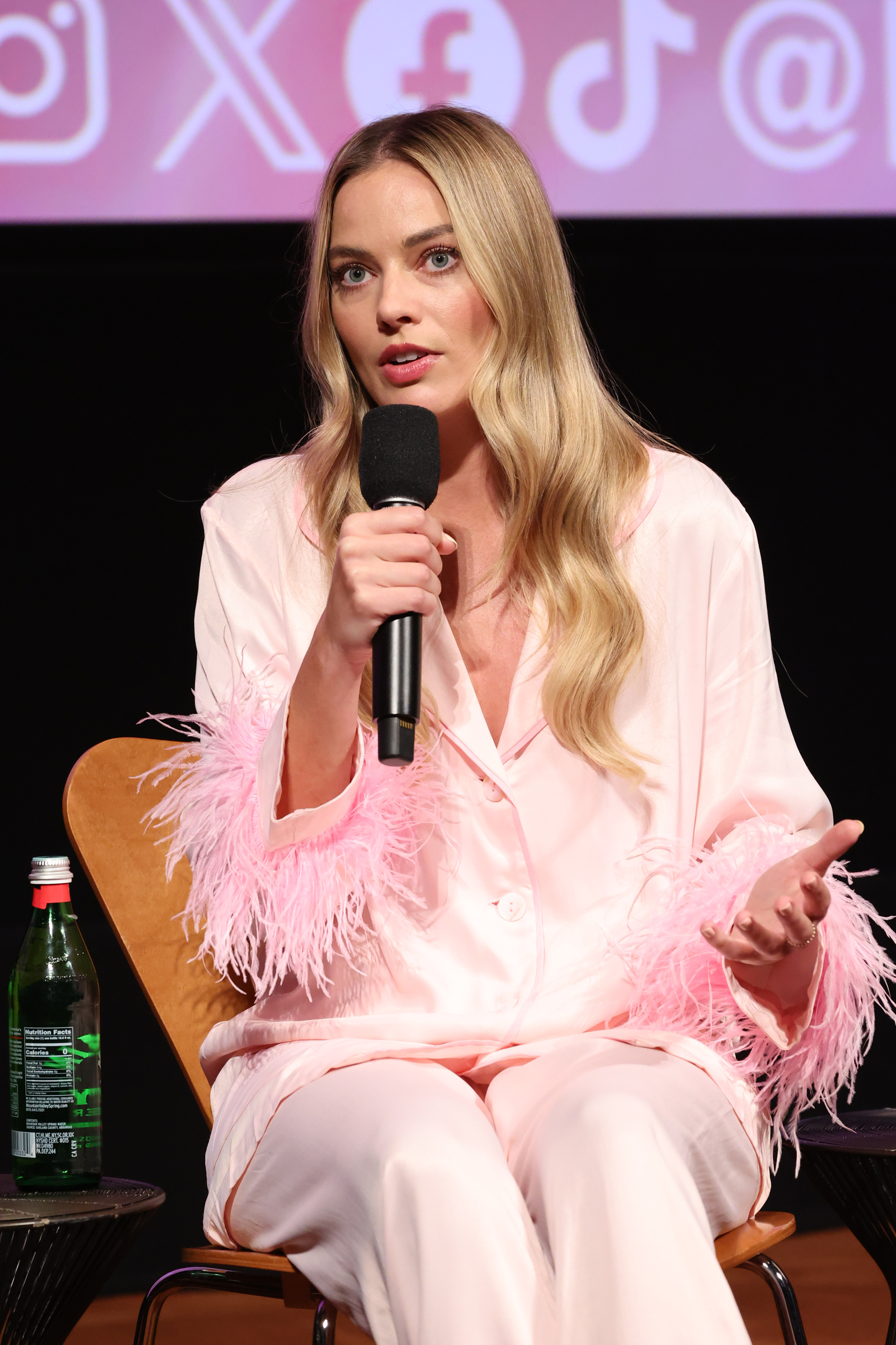 Close-up of Margot holding a microphone and sitting at a media event