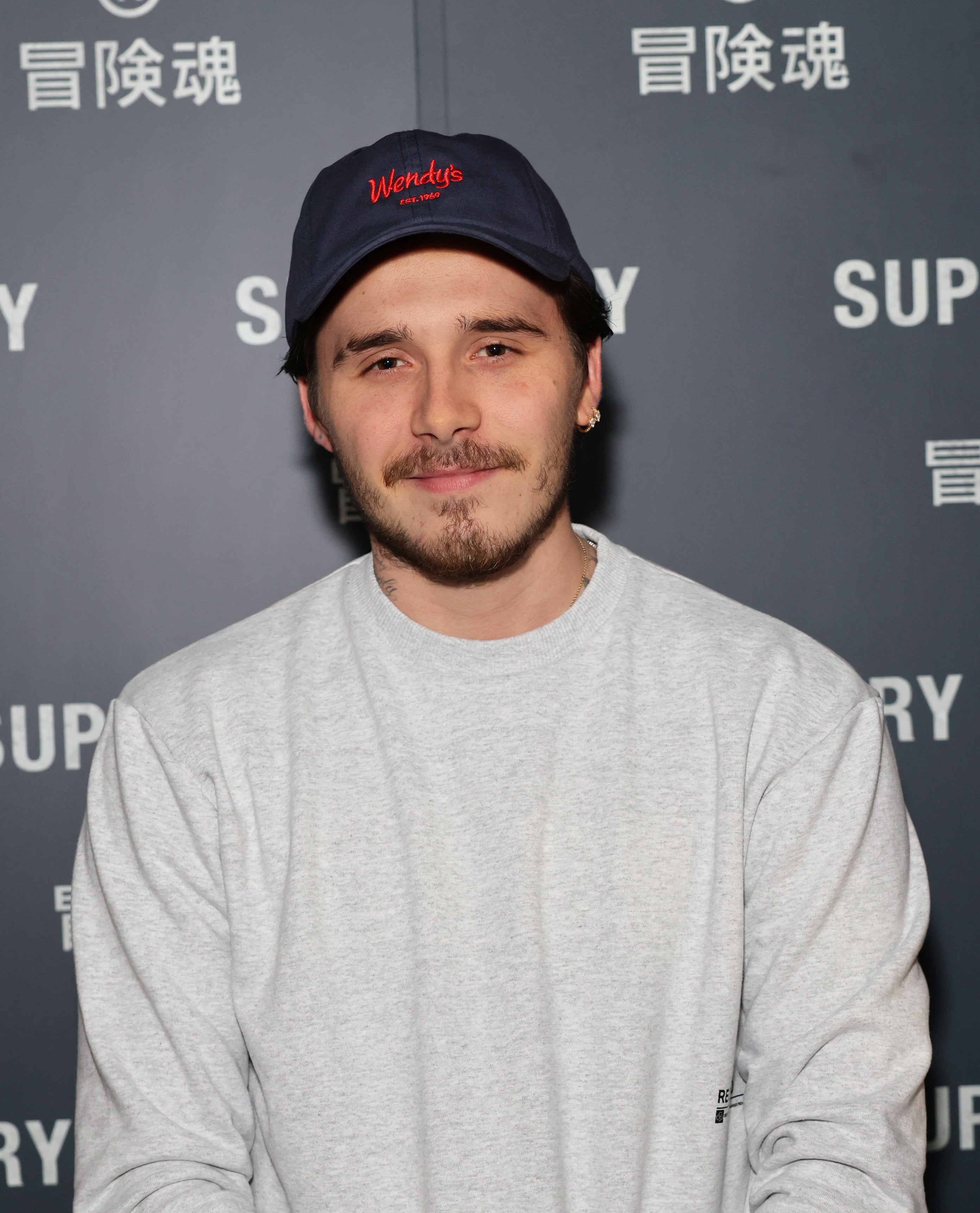 Close-up of Brooklyn at a media event wearing a shirt and cap