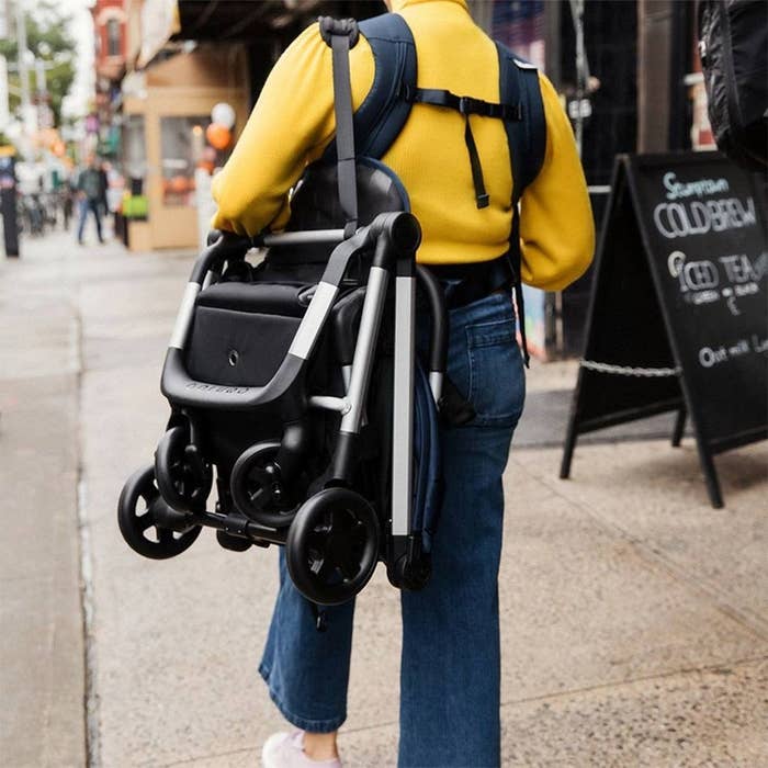 someone walking wearing the collapsed stroller on their shoulder like a tote
