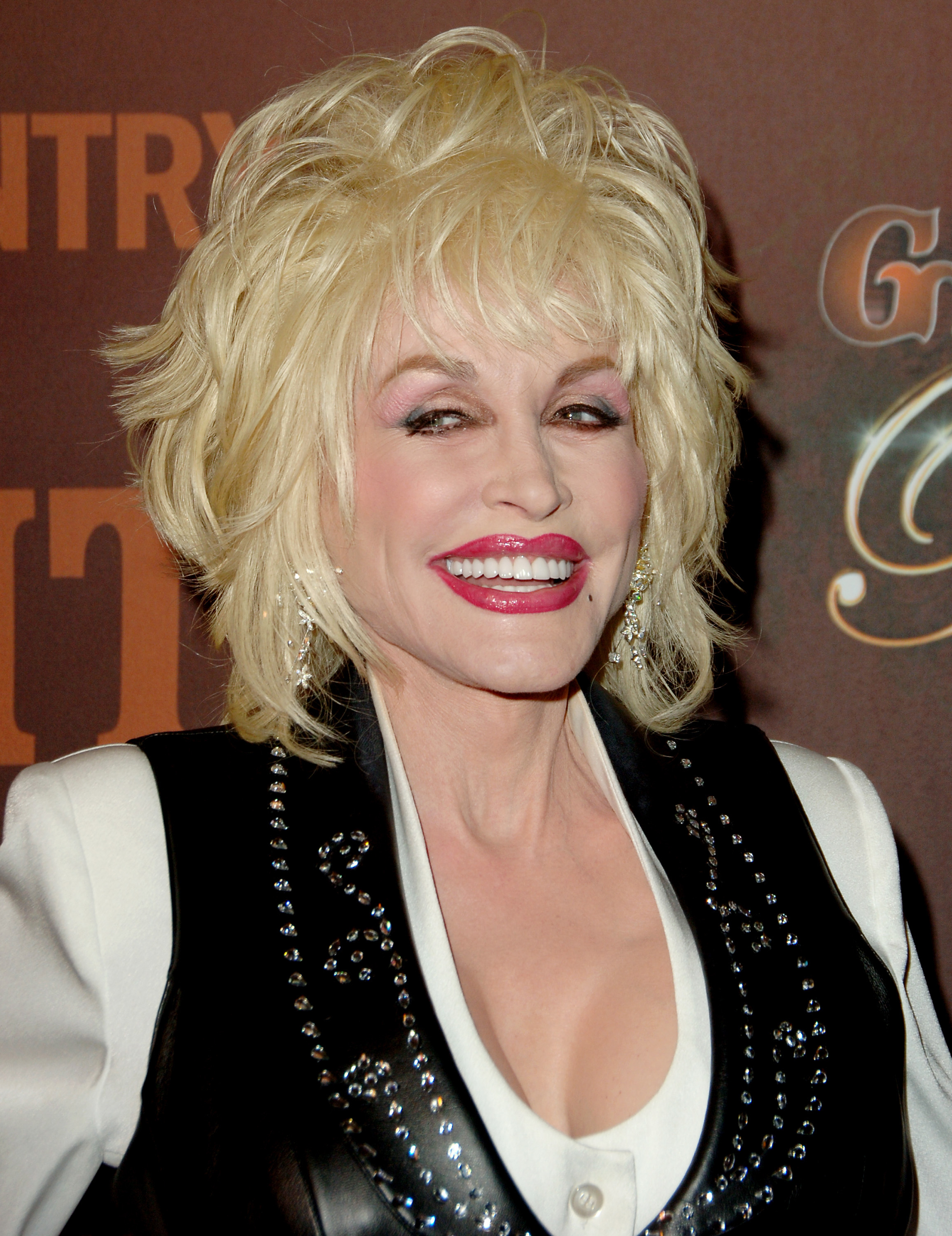 Close-up of Dolly smiling in a vest and blouse at a media event