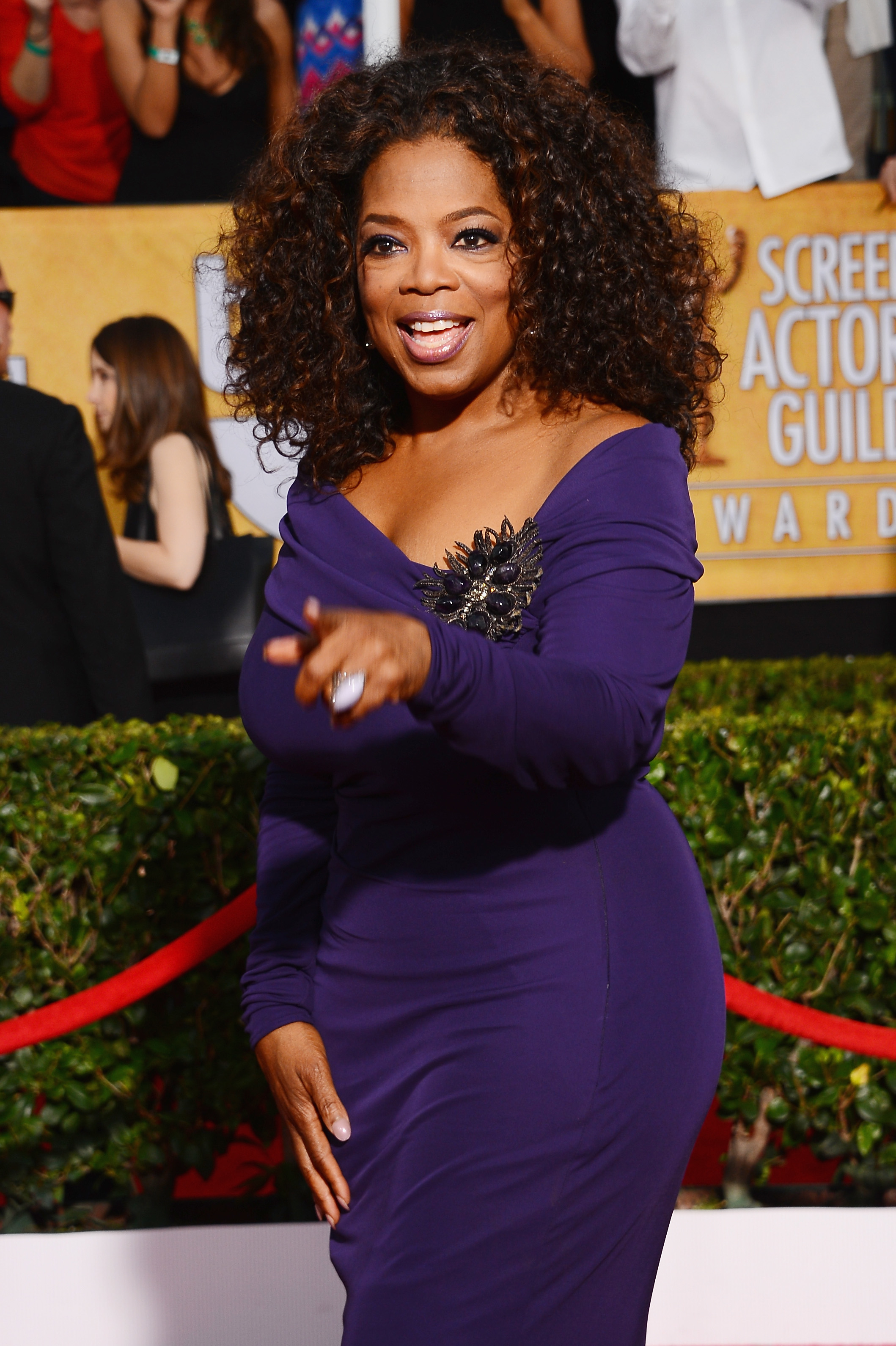 Close-up of Oprah pointing and wearing an off-the-shoulder dress at a media event