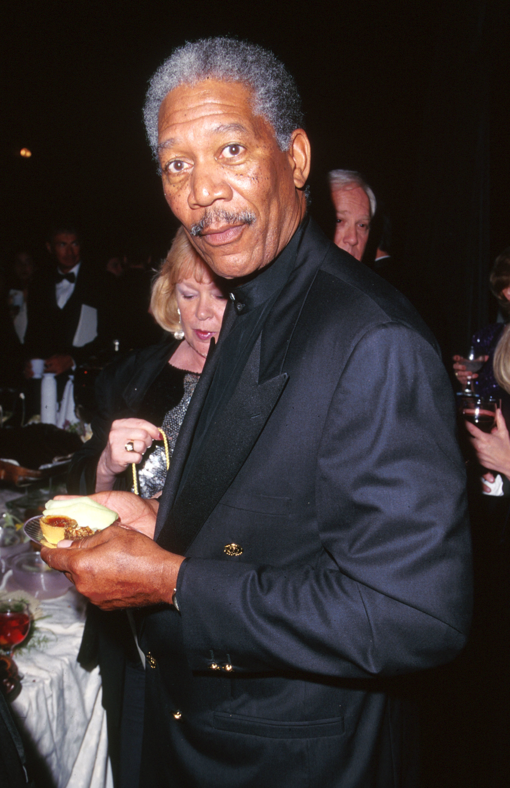 Close-up of Morgan in a suit and holding a small plate of food
