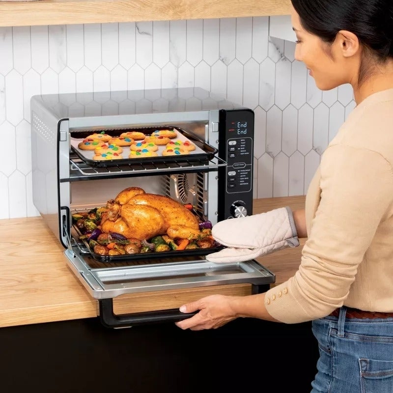model menggunakan oven untuk memasak ayam di bagian bawah dan kue di bagian atas