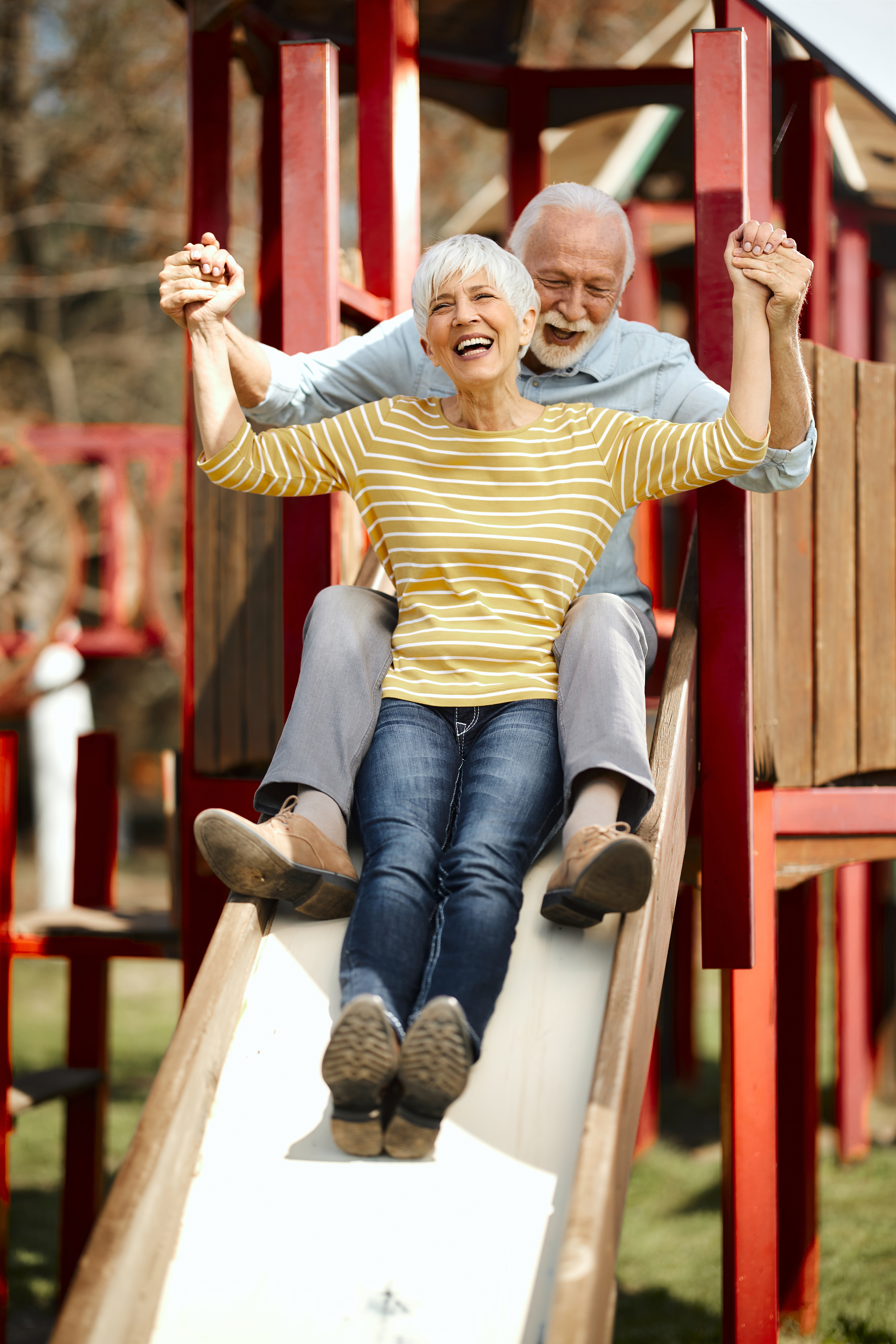 Two smiling older people going down a slide