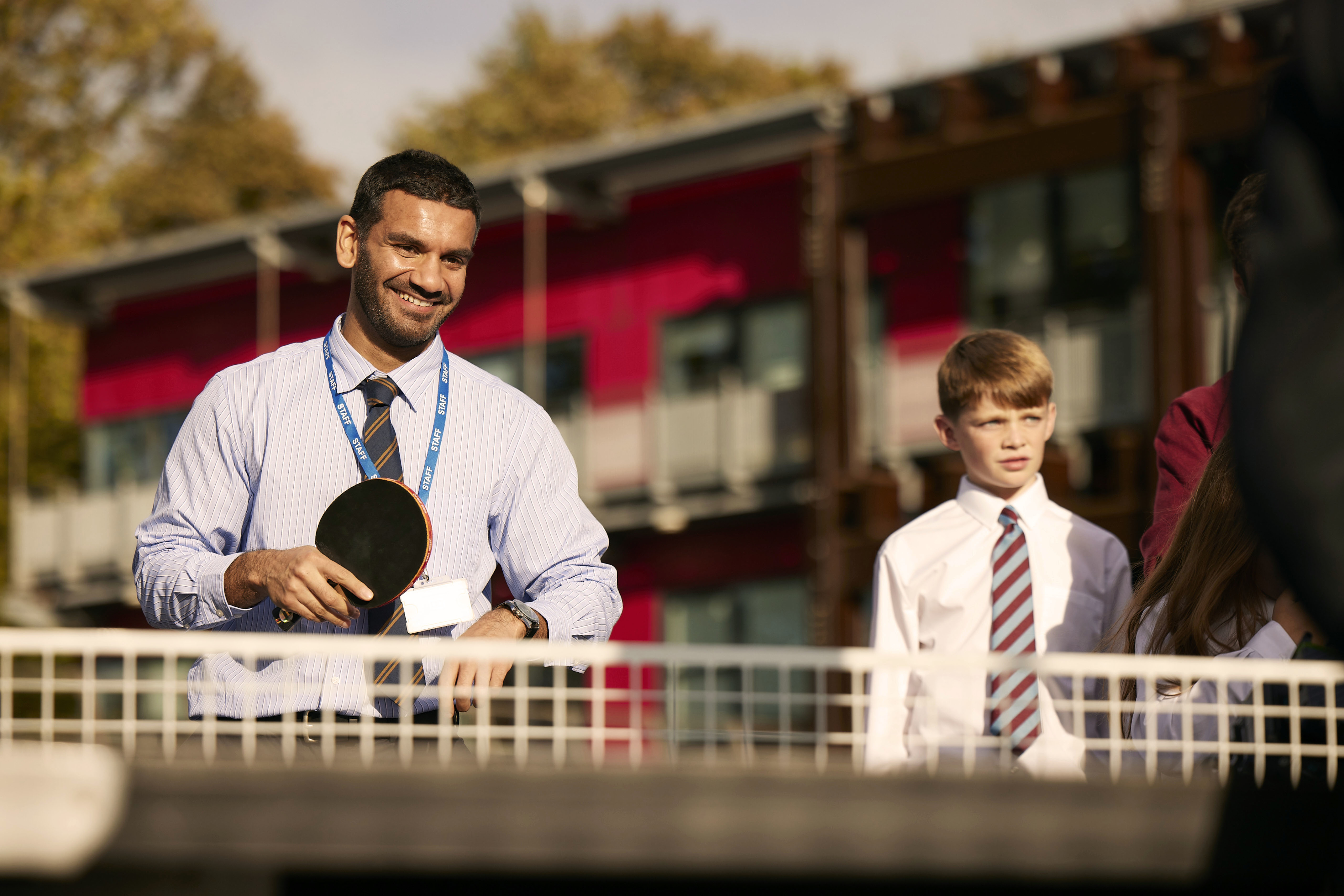 A teacher smiles while playing table tennis with students