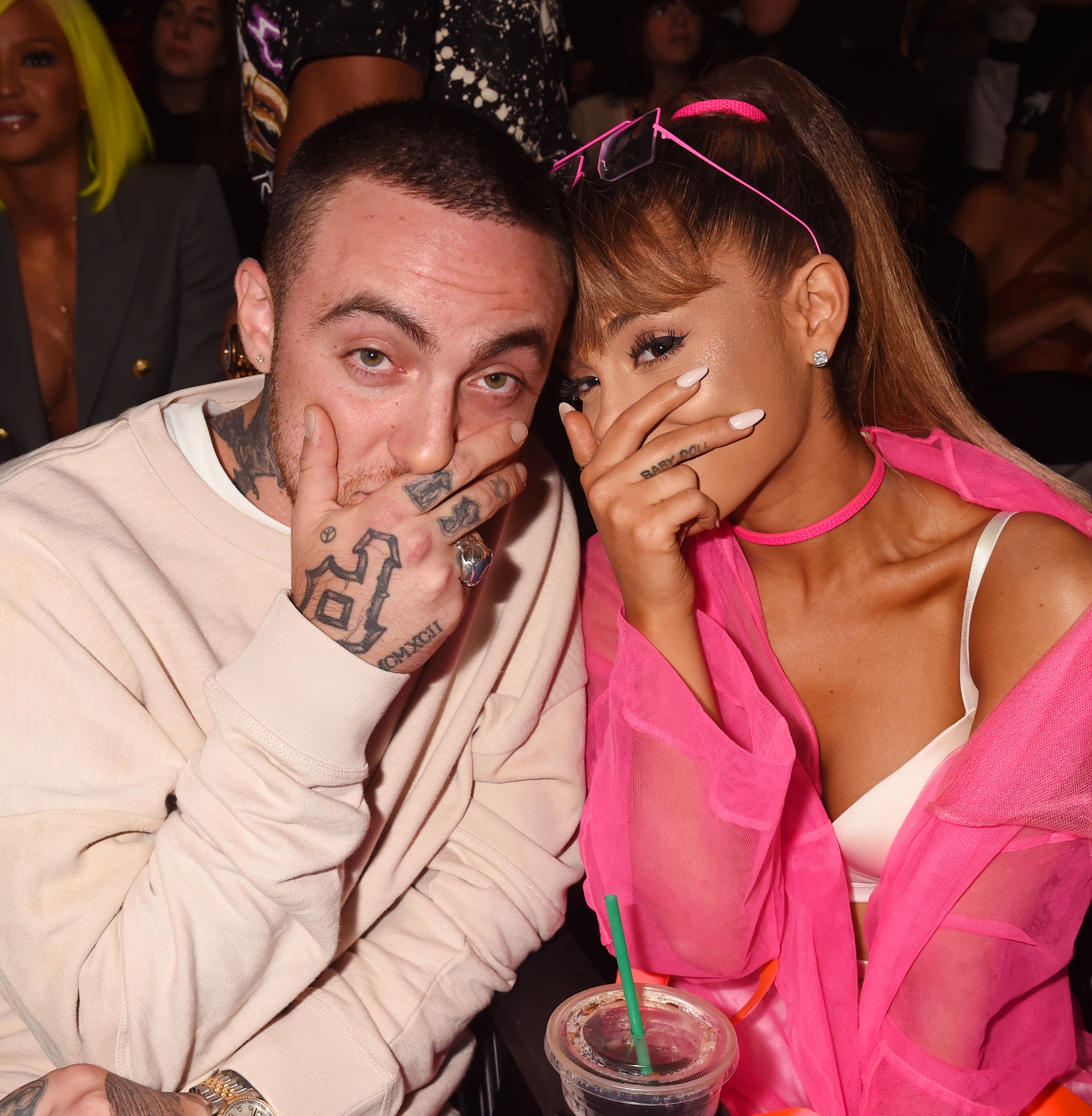 Mac and Ariana sitting together and posing by covering half their face