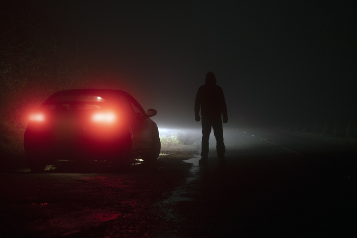 person standing outside of a car on a dark road
