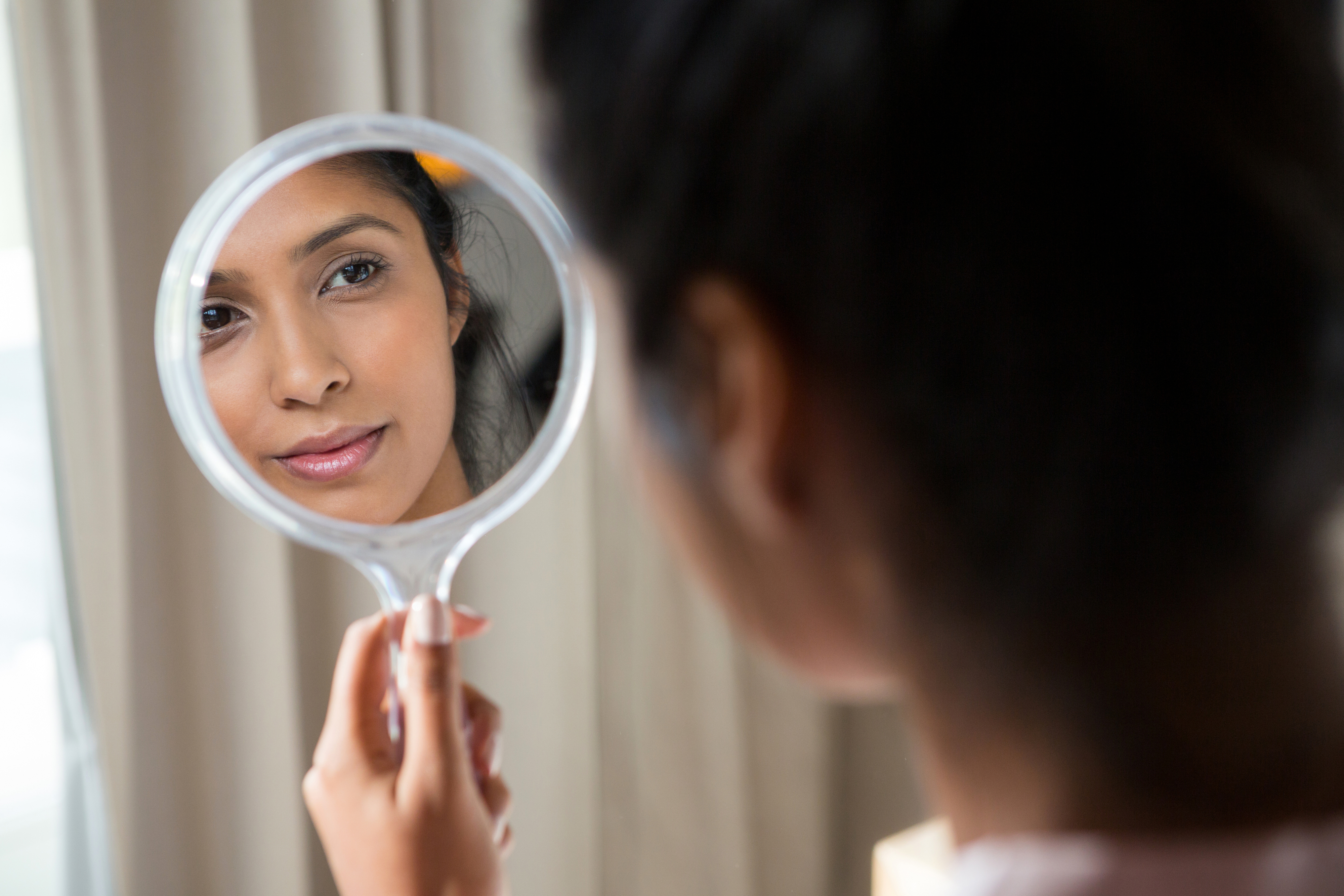 A woman looking at her reflection in a hand mirror