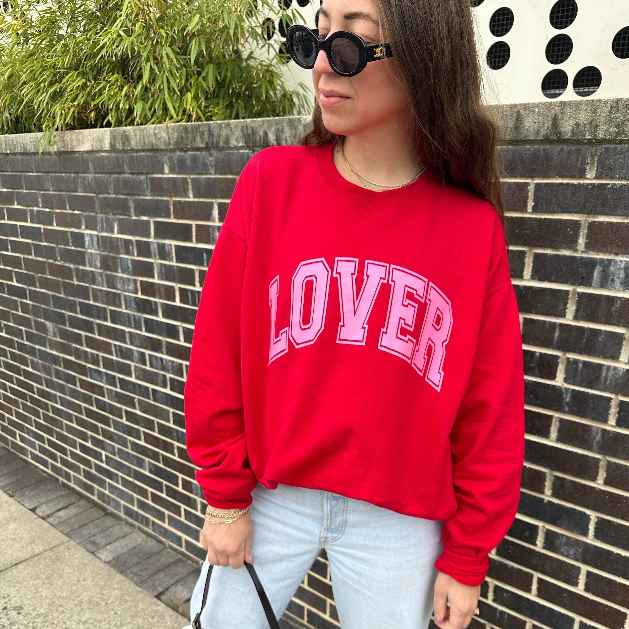 a model wearing a red sweatshirt that says &quot;lover&quot; in pink