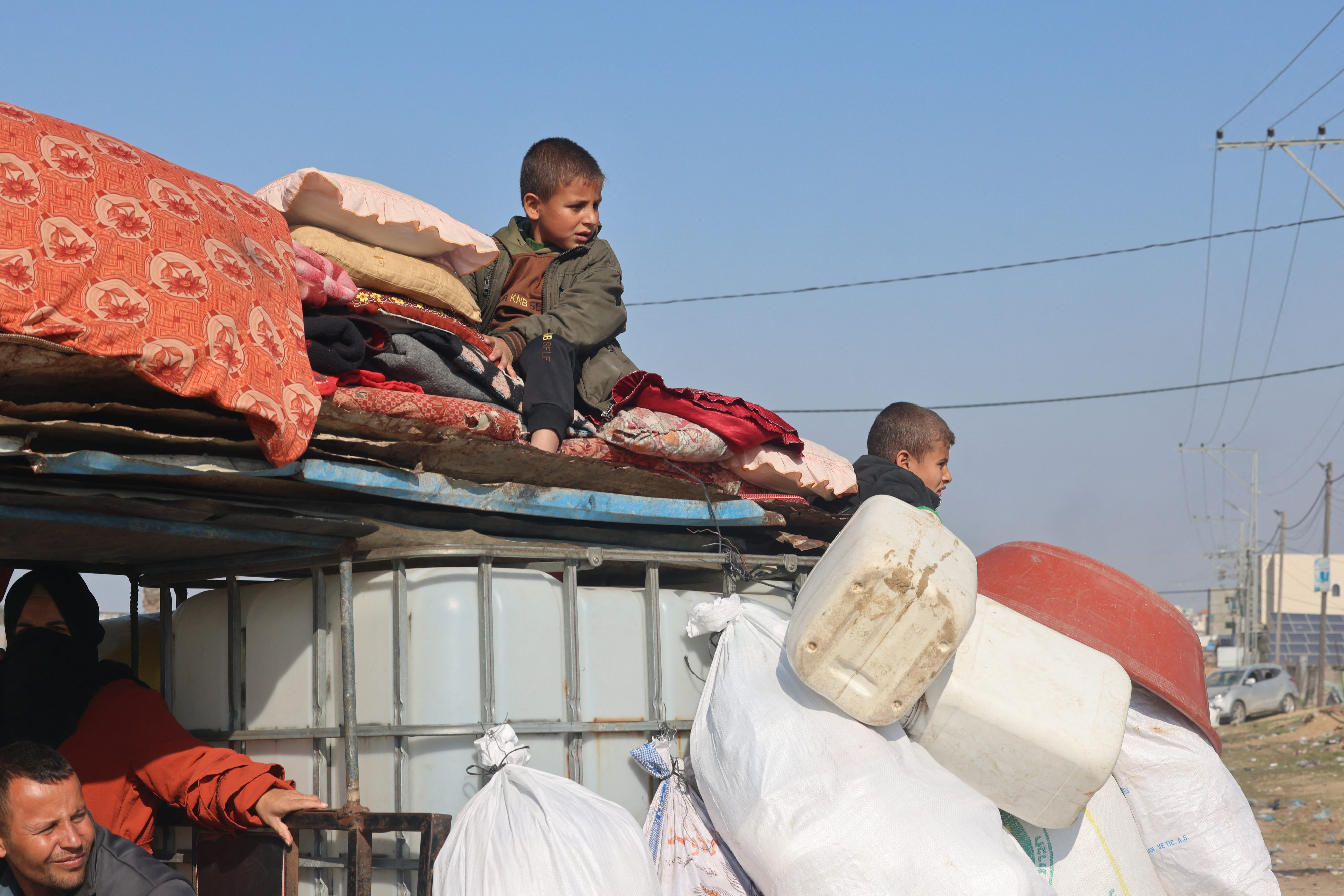 kids sitting on a top of a vehicle carrying empty jugs and pillows