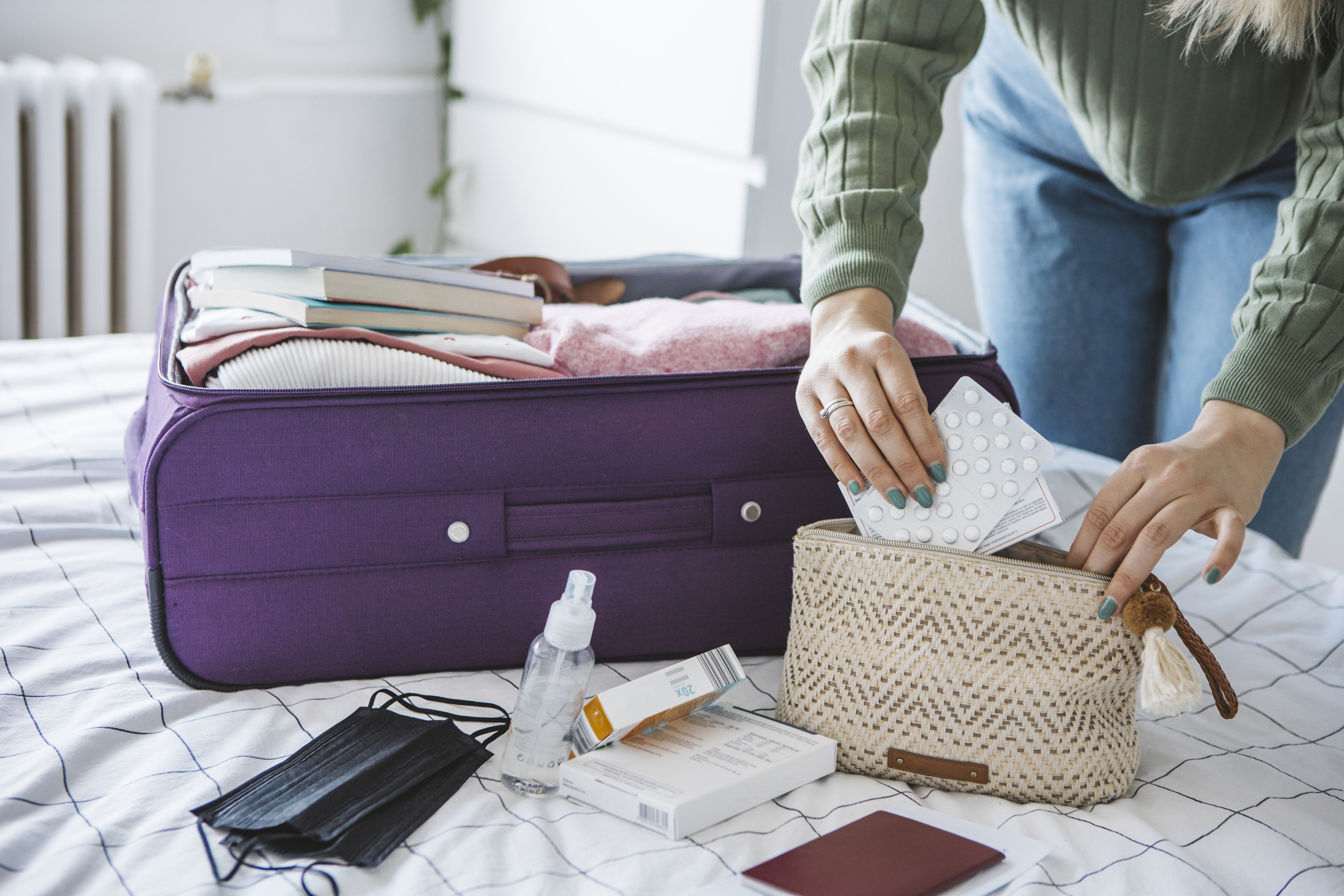 Woman preparing travel suitcase on bed at home with medication