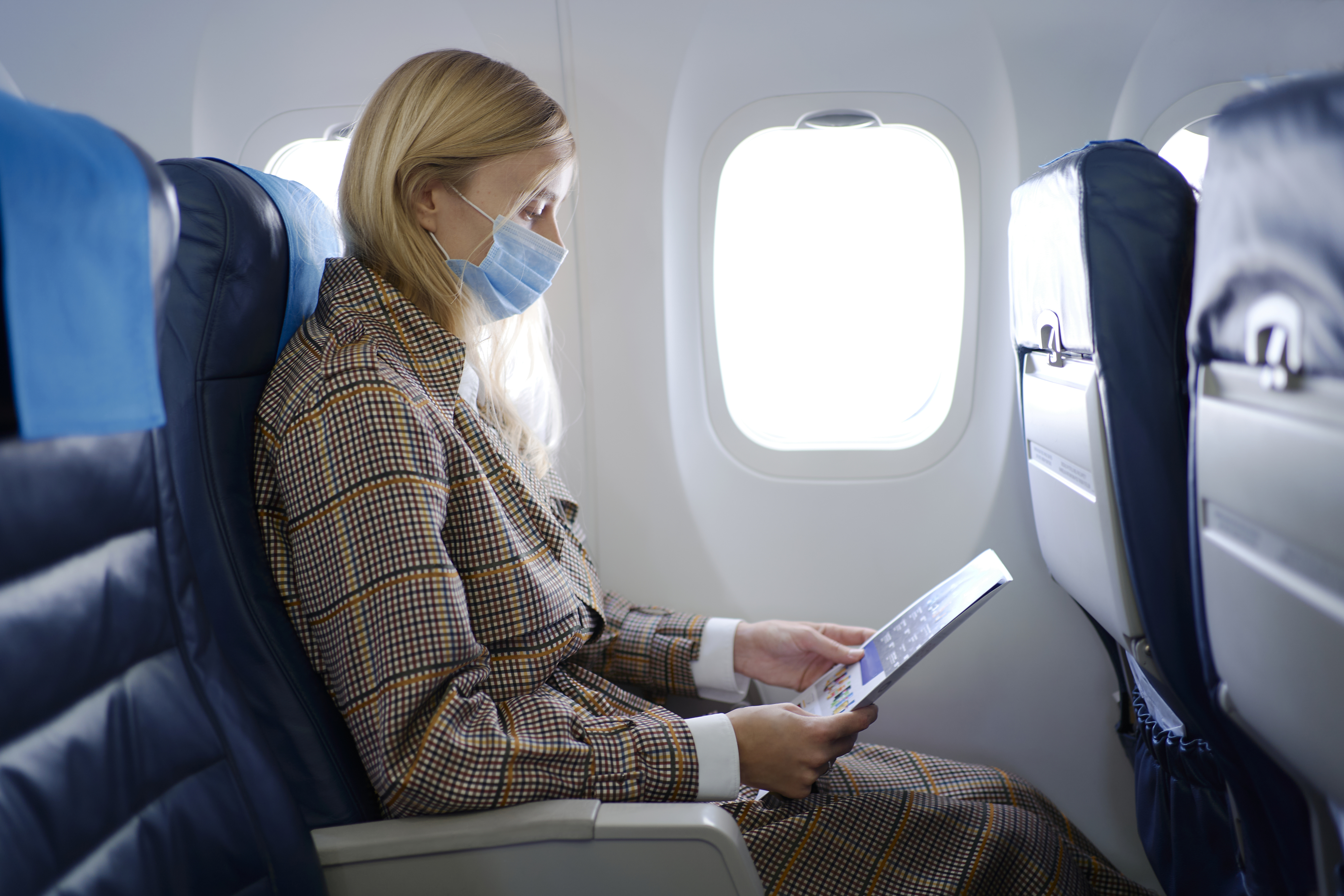 woman reading something in an airplane with a mask over her mouth and nose