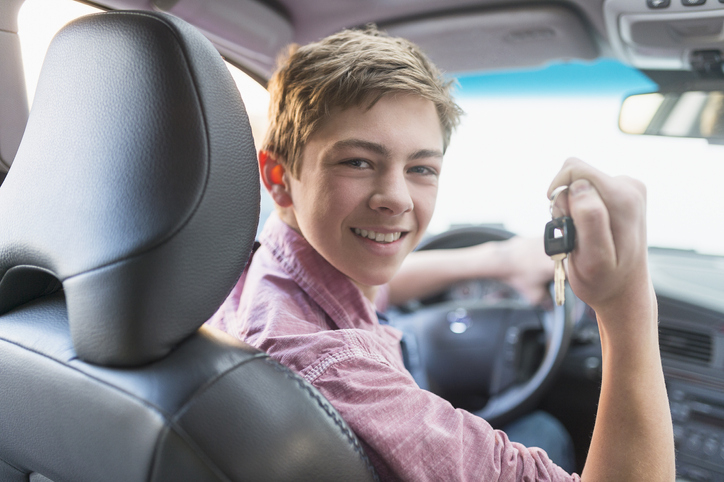 A young teen smiling and holding his car keys while in the driver&#x27;s seat
