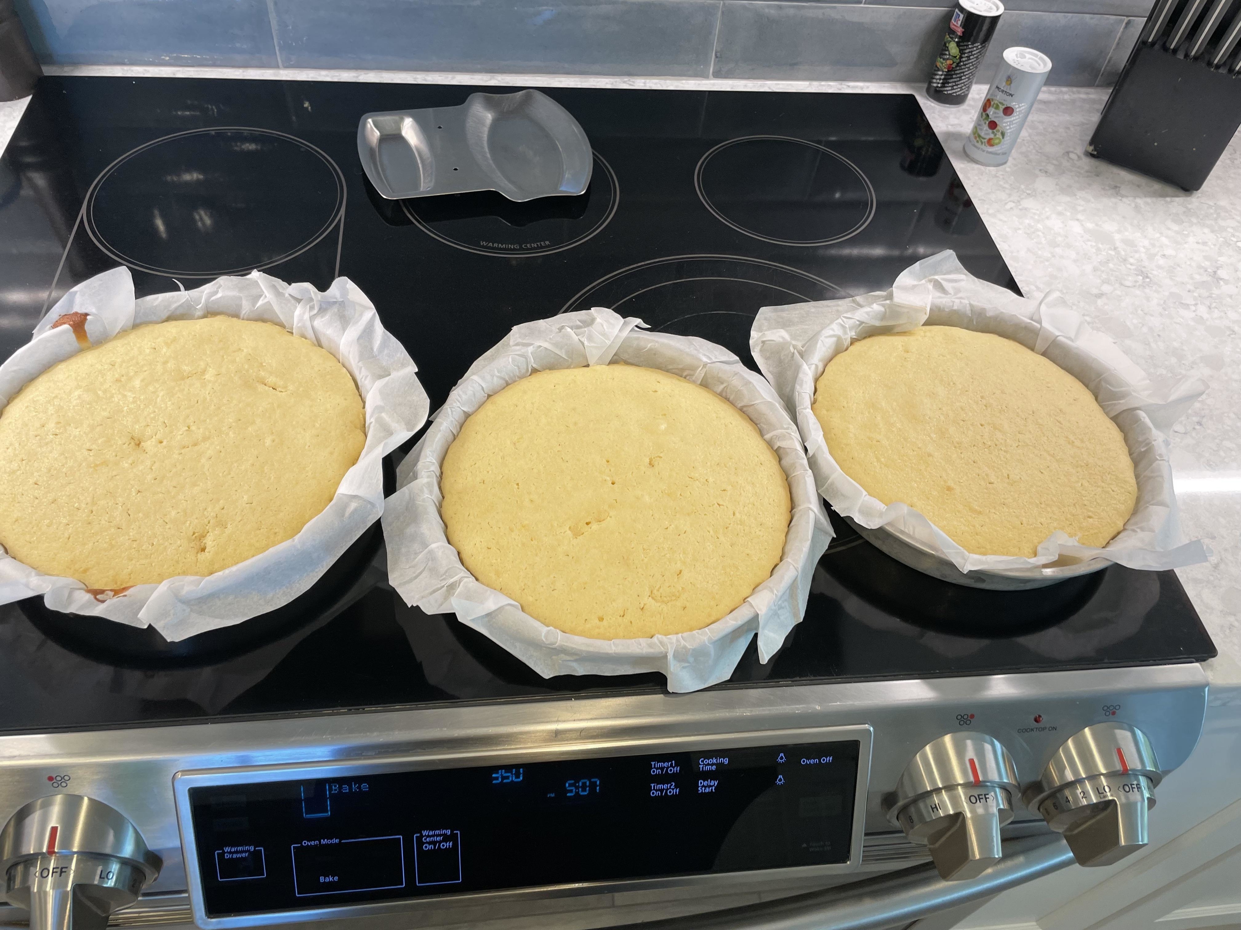 Three baked cakes with parchment sticking out of the tins