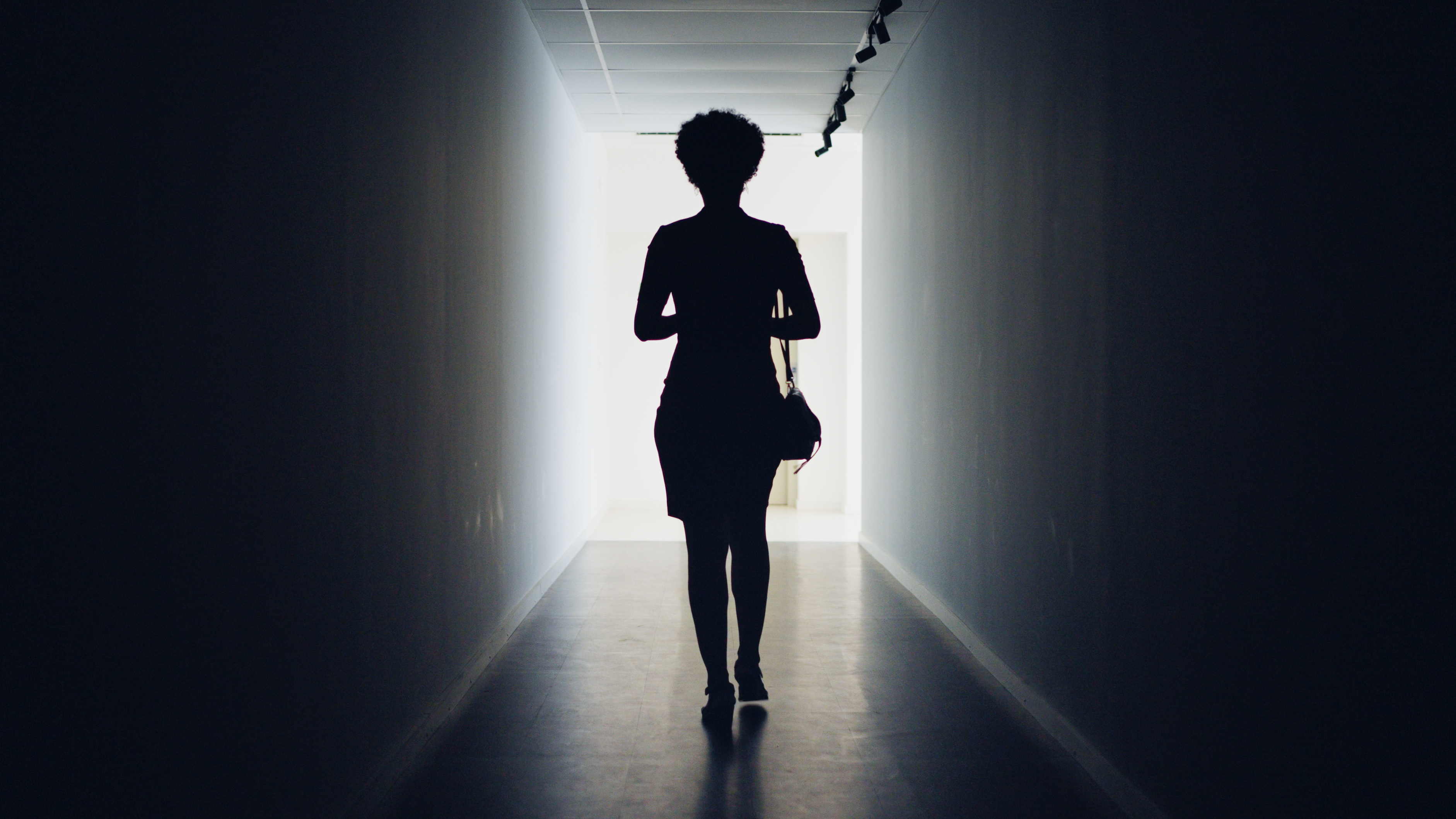 Silhouetted businesswoman walking down a dark corridor to doorway