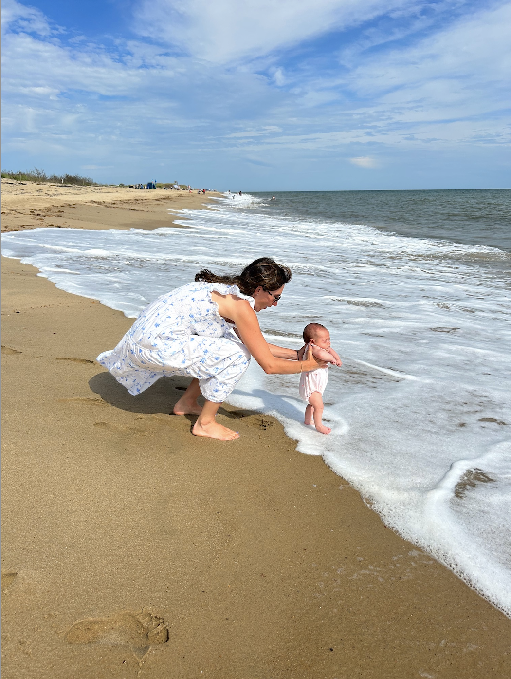 Hannah holding her daughter&#x27;s feet in the water at the beach