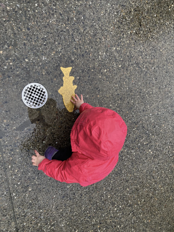 A child touching a painted fish on the sidewalk