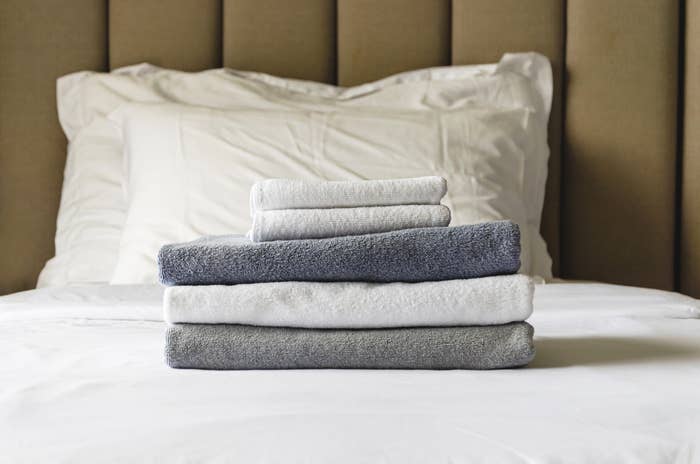 stack of folded terry towels lies on a clean white bed. Cleaning in the guest room of the hotel, cleanliness, laundry, hygiene.