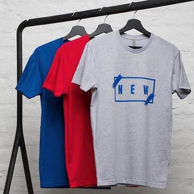 a rack with three T-shirts in different colors hanging on it with the front-most one featuring a graphic that says "new"