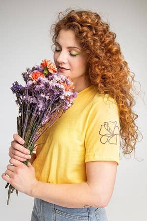 a model holding a bouquet of flower while wearing a yellow T-shirt with a flower embroidered on the sleeve