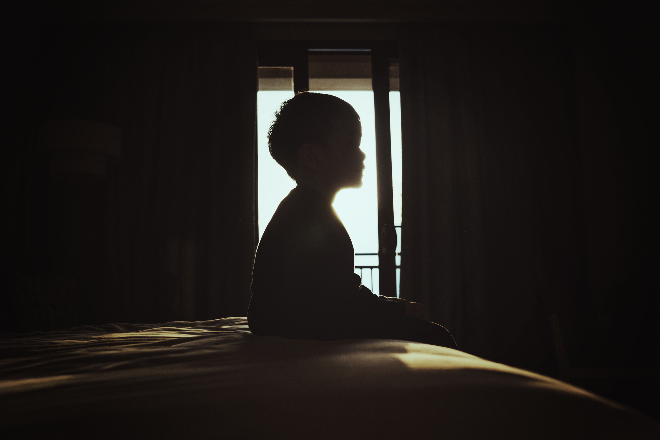 A boy sitting in a dark bedroom