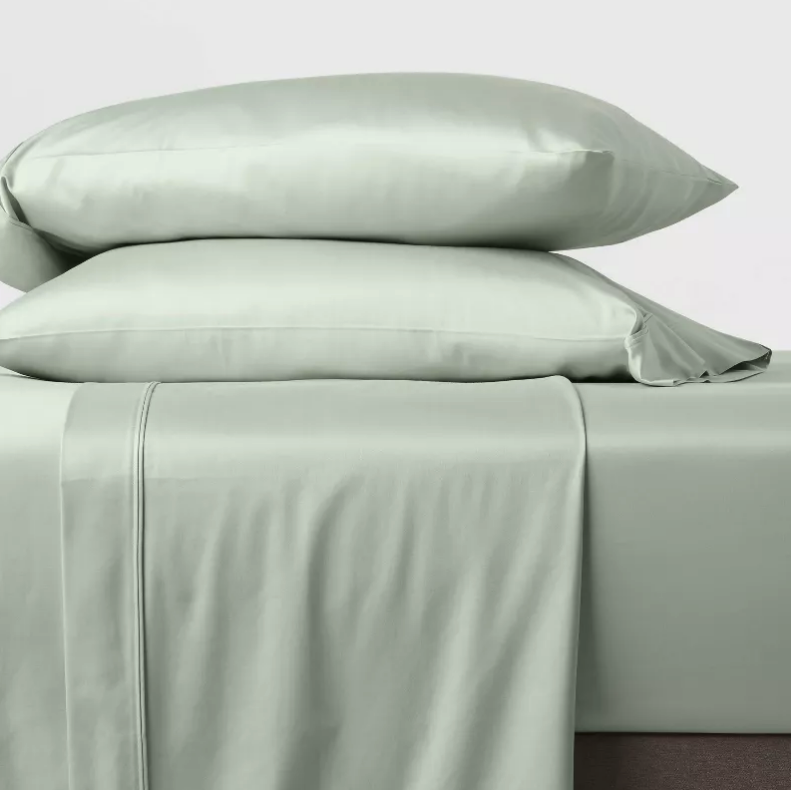 a bed with green sheets and pillow with green pillowcases stacked on it