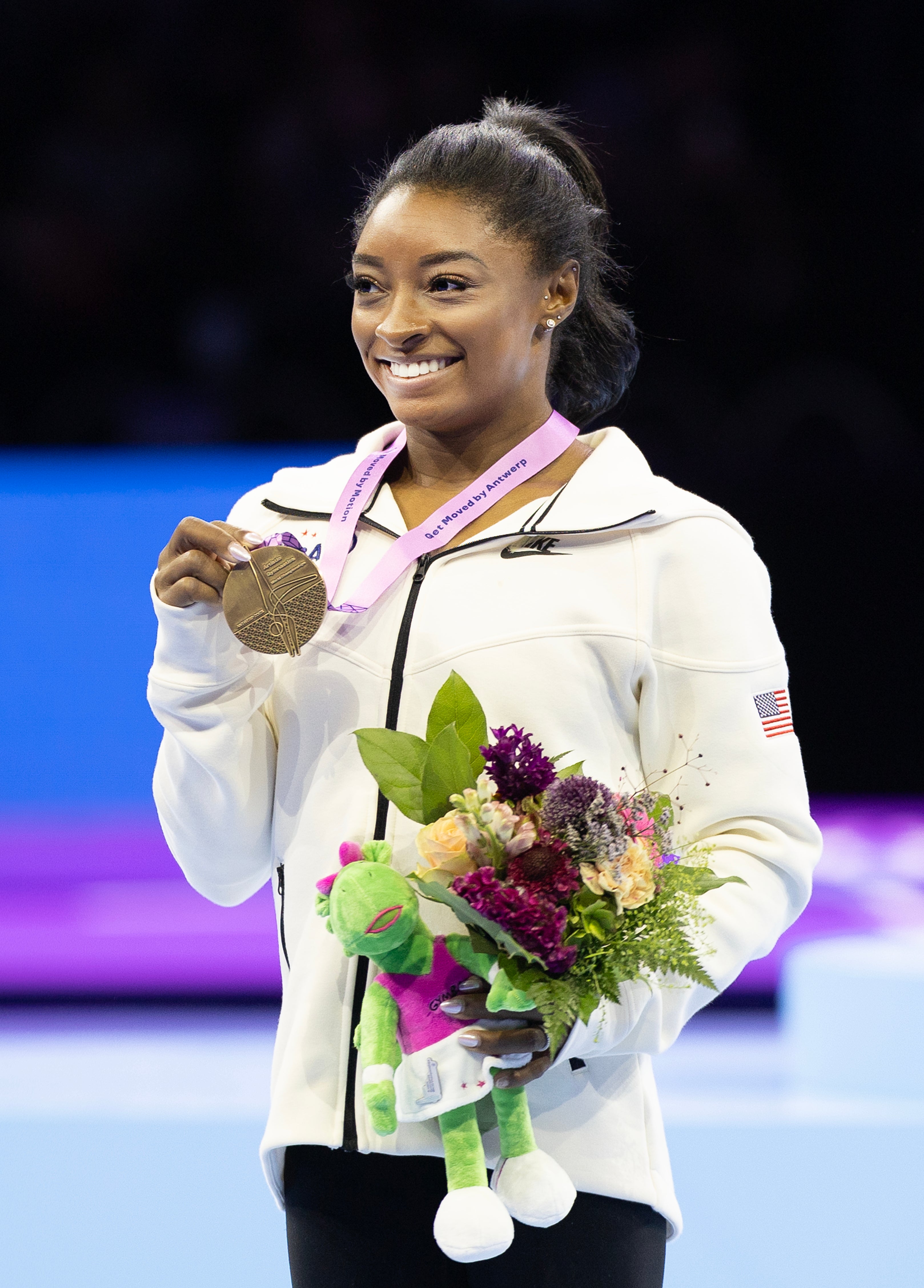 Simone holding out her medal as she holds a bouquet of flowers at the Olympics
