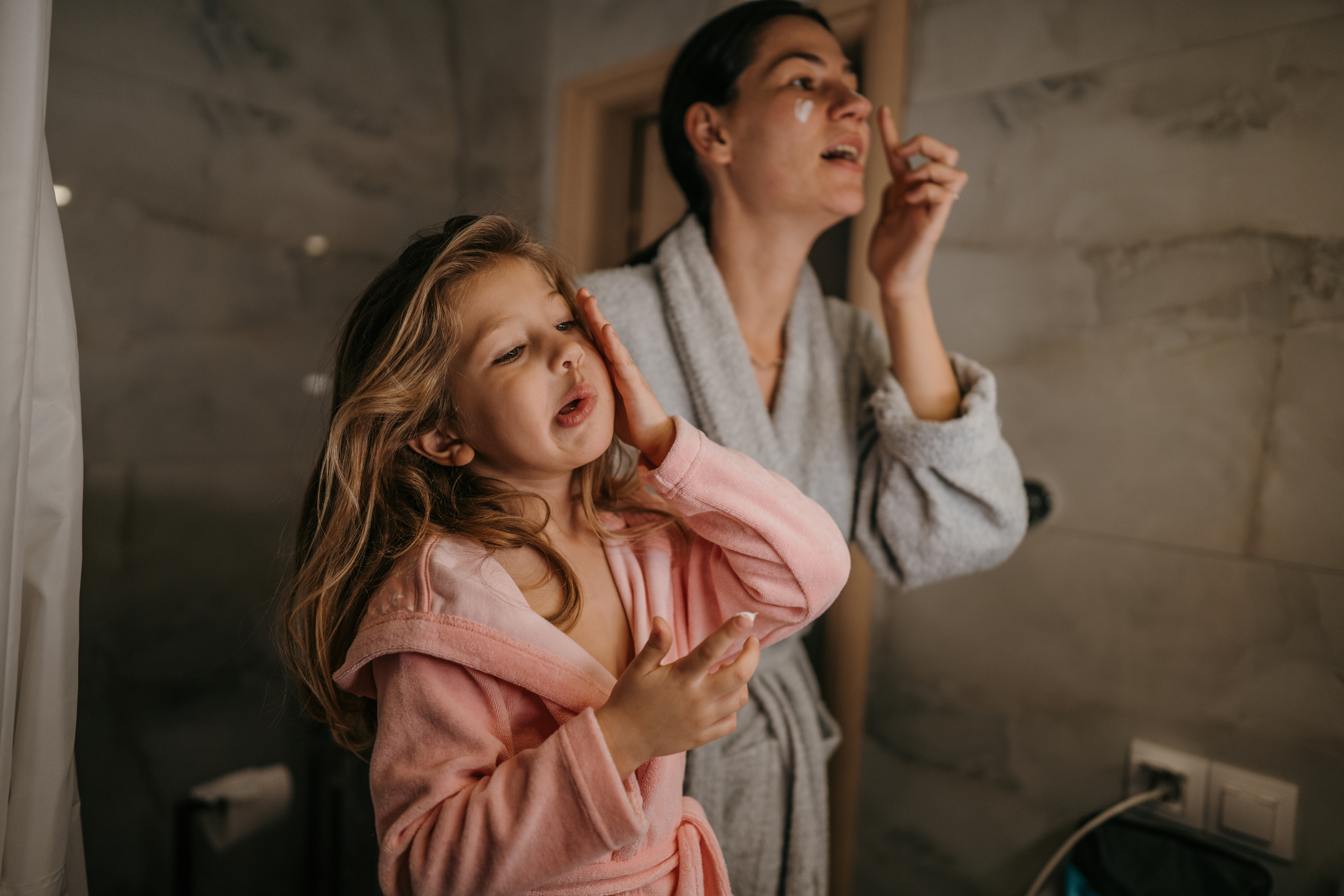 young girl and her mother doing skincare side by side in the bathroom