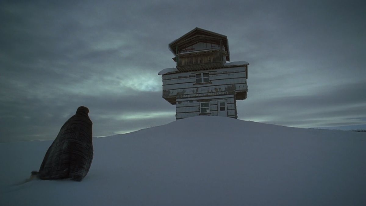 Riley Keough approaching a cross-shaped building buried in snow.