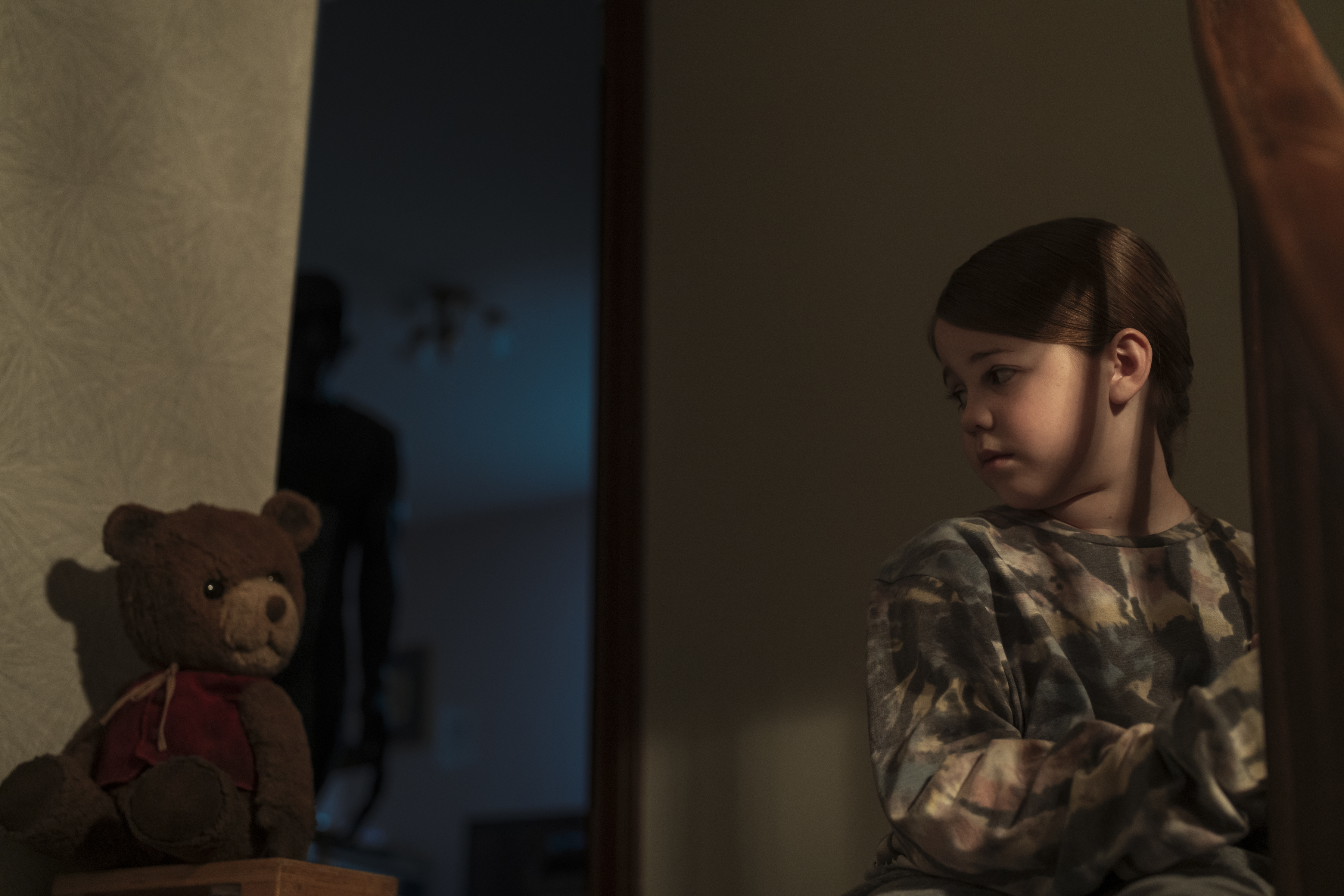 in a dark room a child looks suspiciously at her stuffed teddy