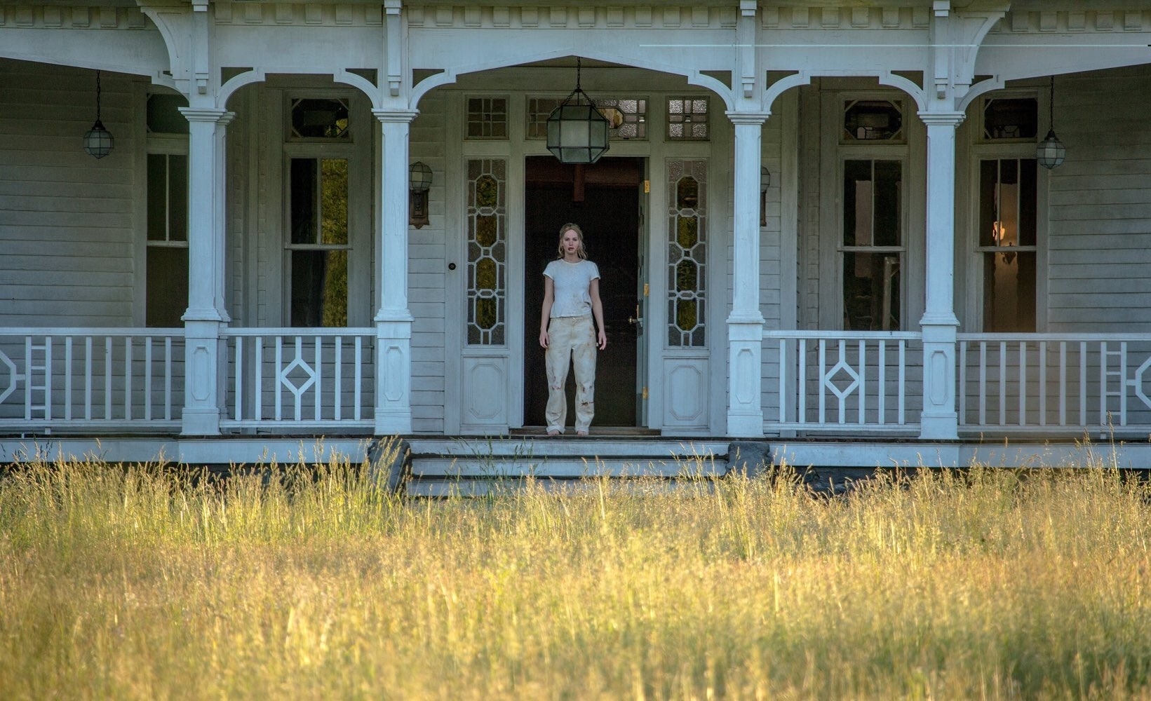 Jennifer Lawrence standing on the front porch of a large house.