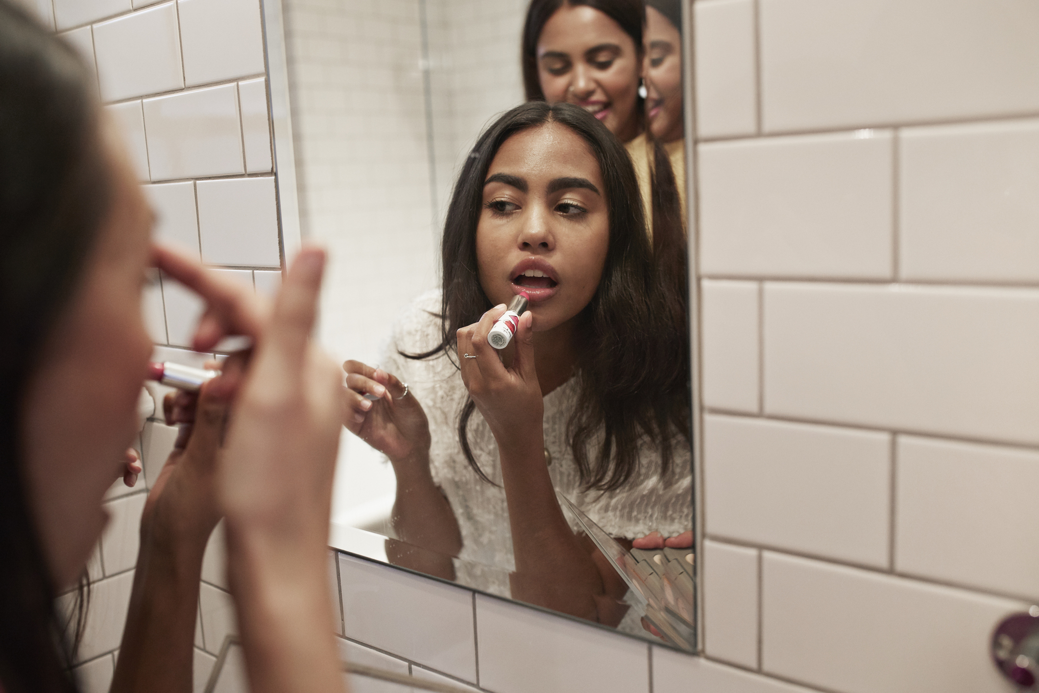 A woman is applying lipstick in front of a mirror