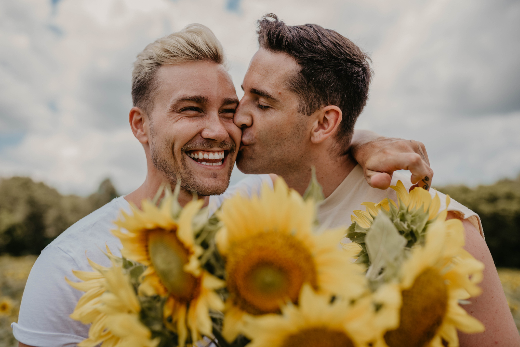 A happy-looking couple is holding a bouquet of sunflowers