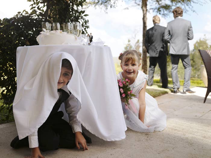 Two kids at a wedding are hiding under a table