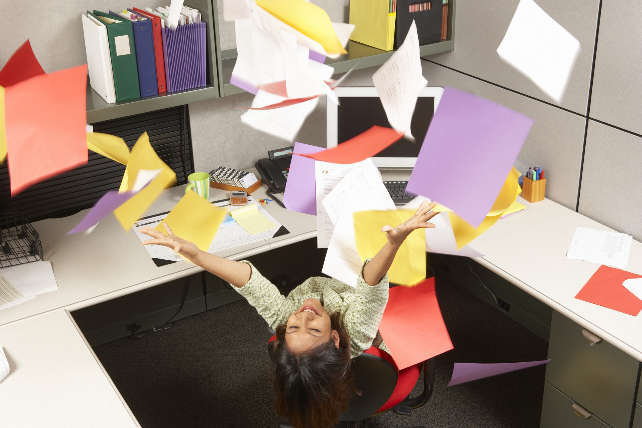 A woman in a cubicle throwing papers in the air