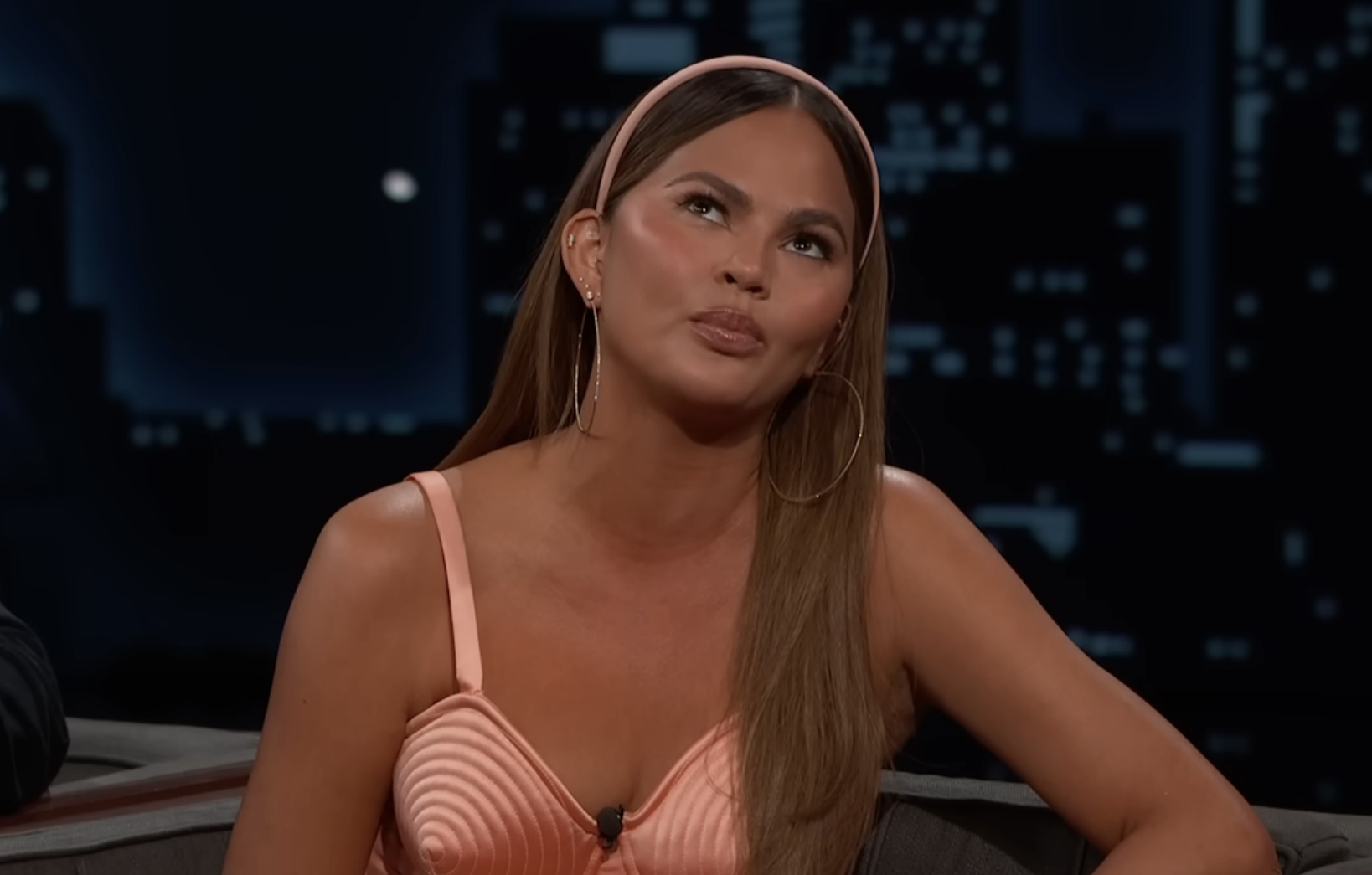 Chrissy sitting on the talk show wearing a spaghetti-strap outfit
