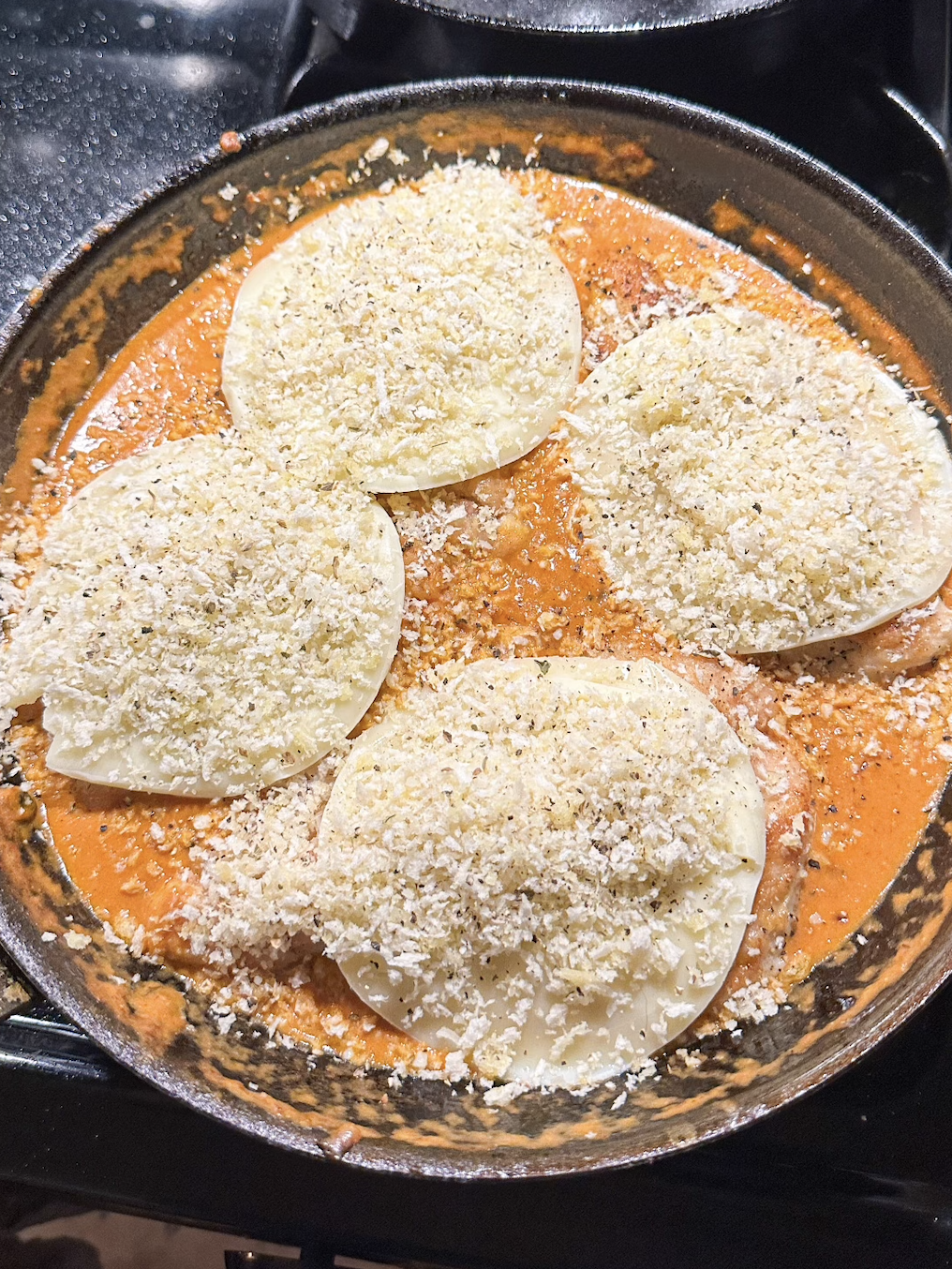 The chicken Parm with slices of cheese on top in a pan before baking